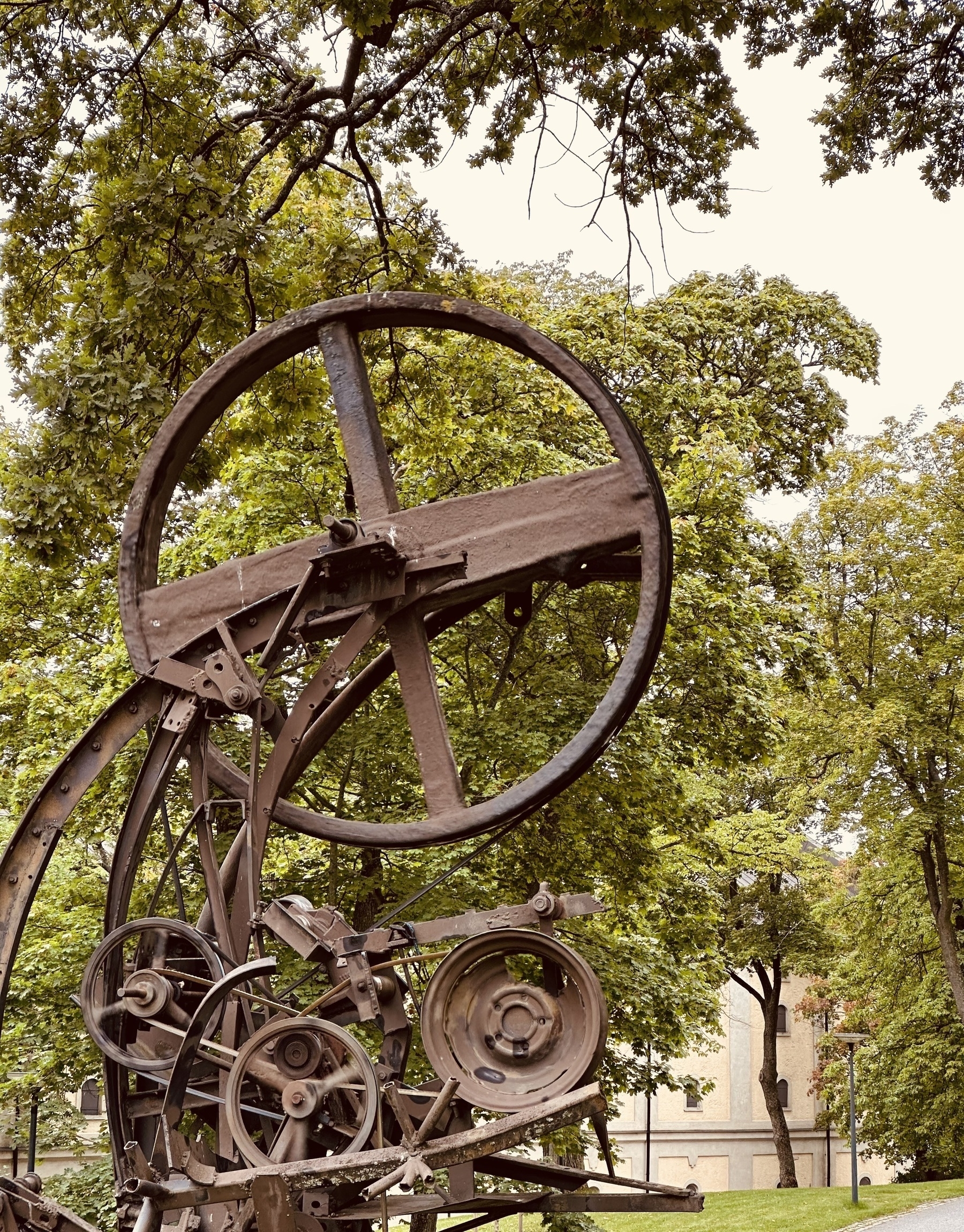 A series of brown metal wheels connected by belts, with trees in the background.