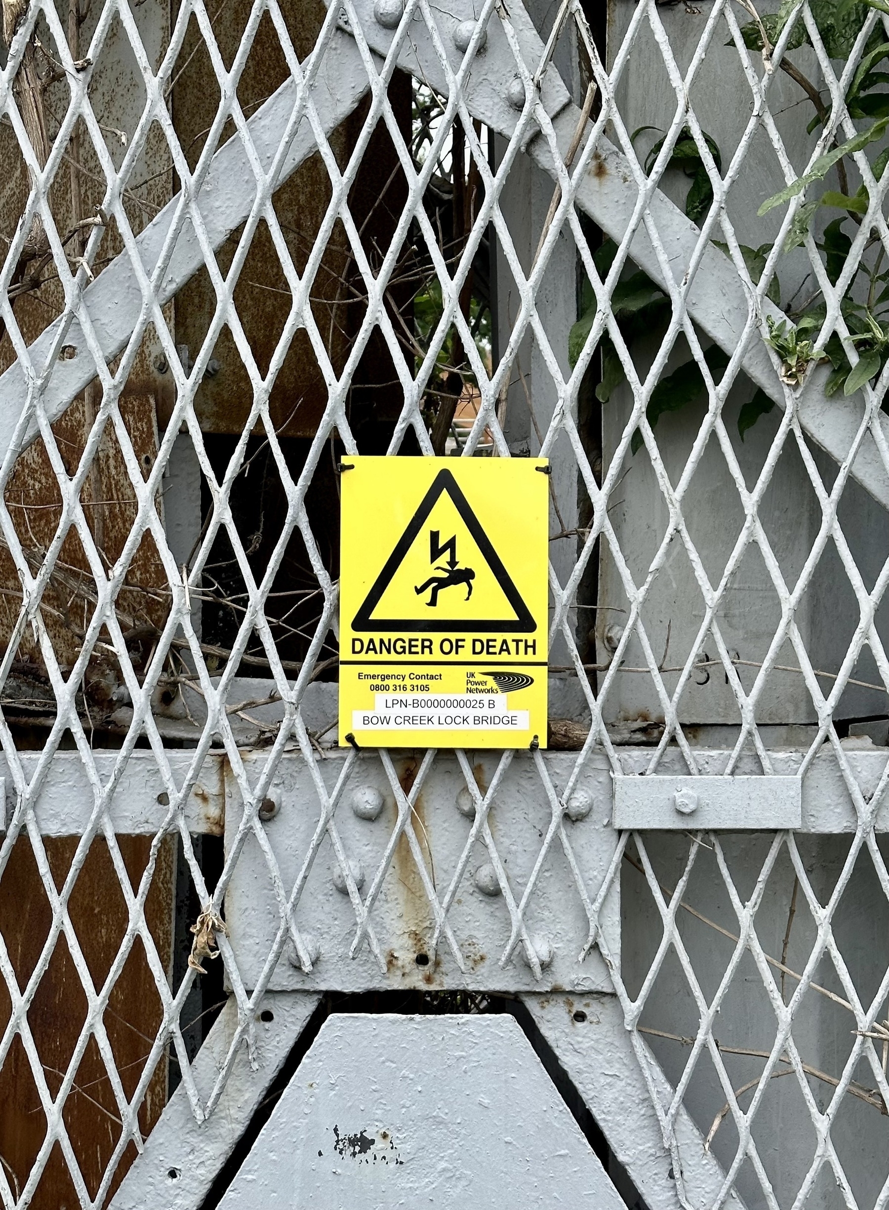 A yellow sign that says danger of death on a grey metal grating.