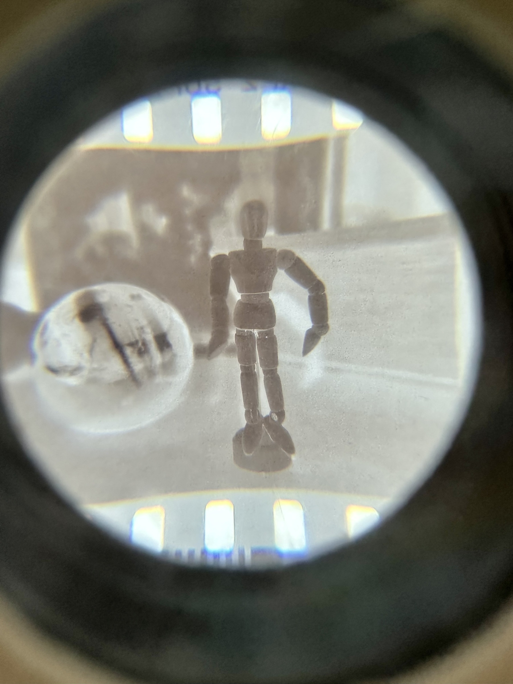 A negative of a photo of a wooden figure of a human, seen through a magnifying loupe.