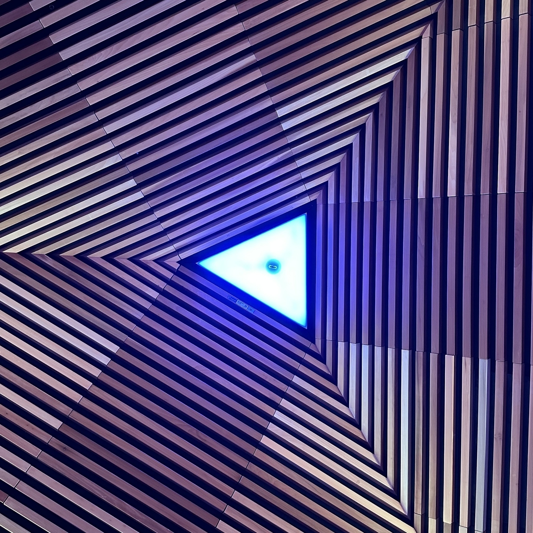 A triangular light surrounded by concentric wooden triangles.