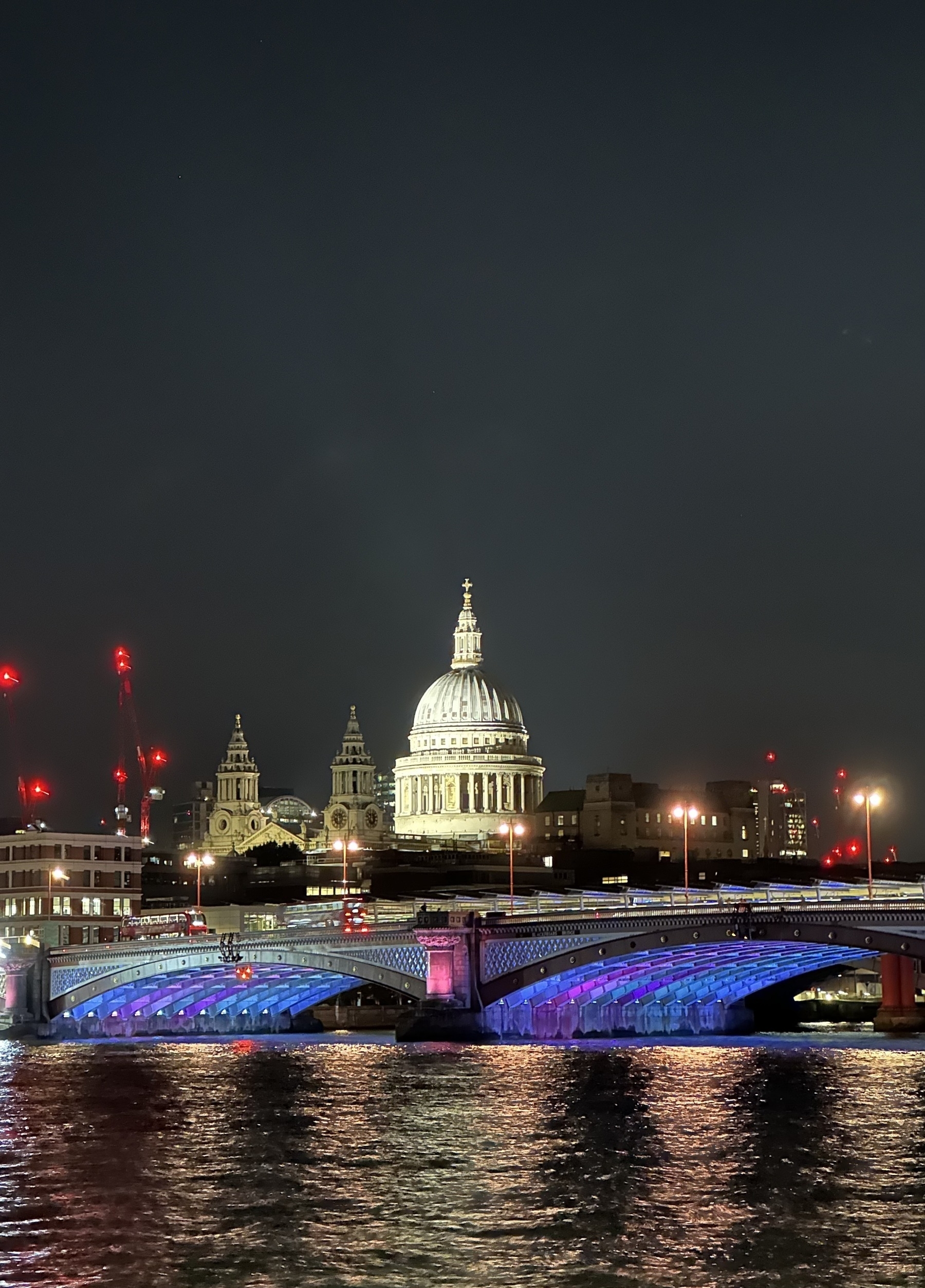 The dome of St Paul’s cathedral lit up at night, seen from across the river Thames, with Blackfriars’s bridge in the foreground.