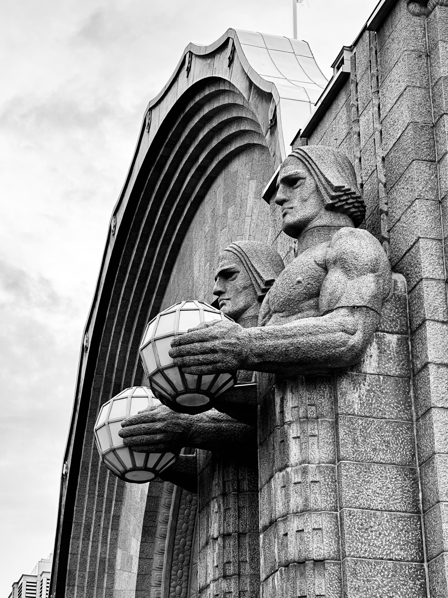 Two large stone statues holding polygonal orbs. On the front of Helsinki Central Station.