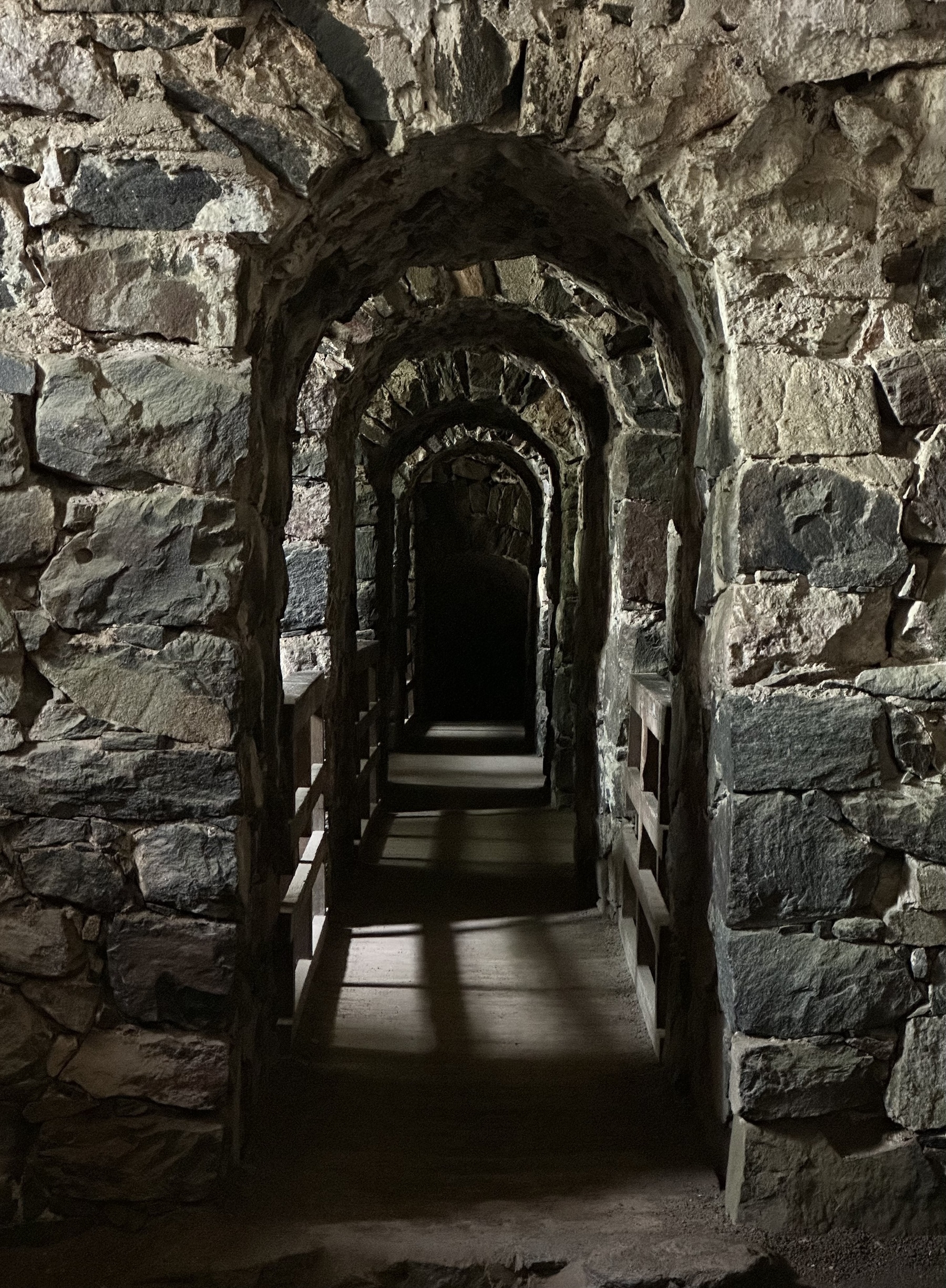 A series of stone arches over a walkway, leading off in to the darkness.