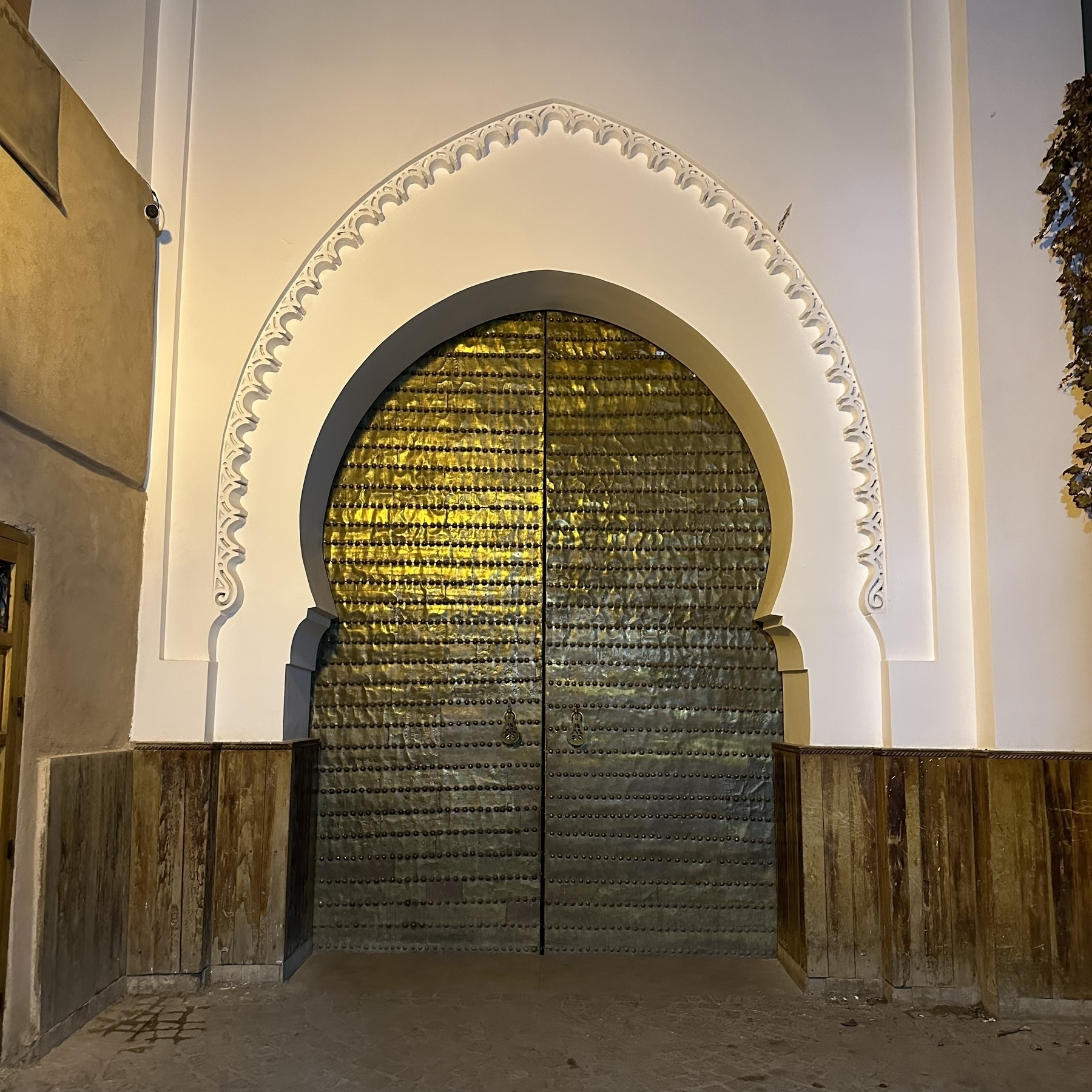 Studded bronze doors, closed, in a white arch.