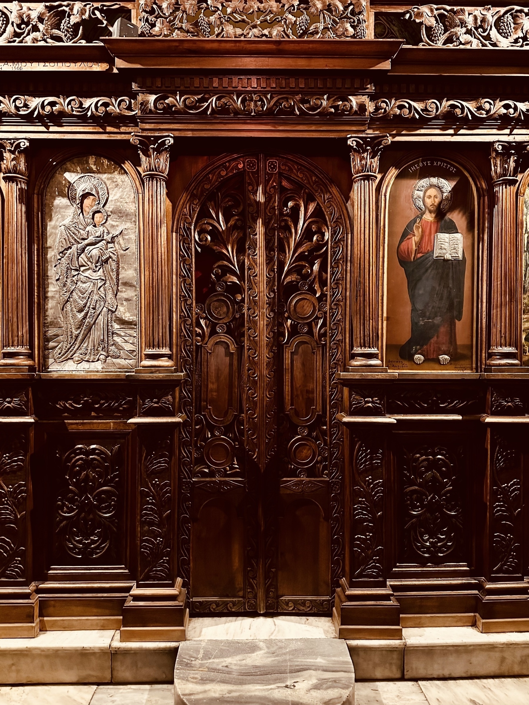 An ornately carved arched wooden door in a carved wooden wall, with religious icons to the left and right of it.