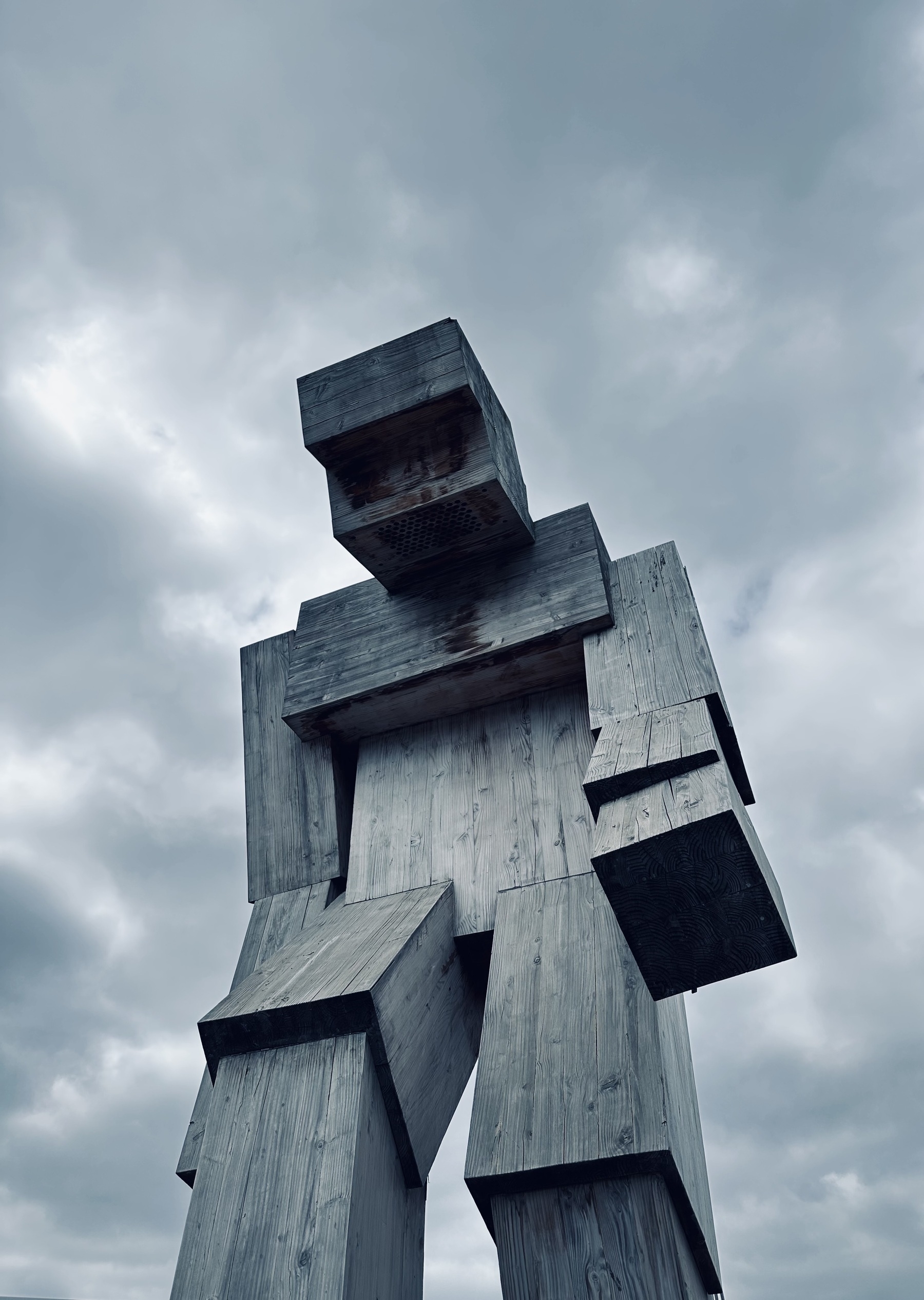 A large blocky figure of a person, made of wood. Cloudy sky in the background.