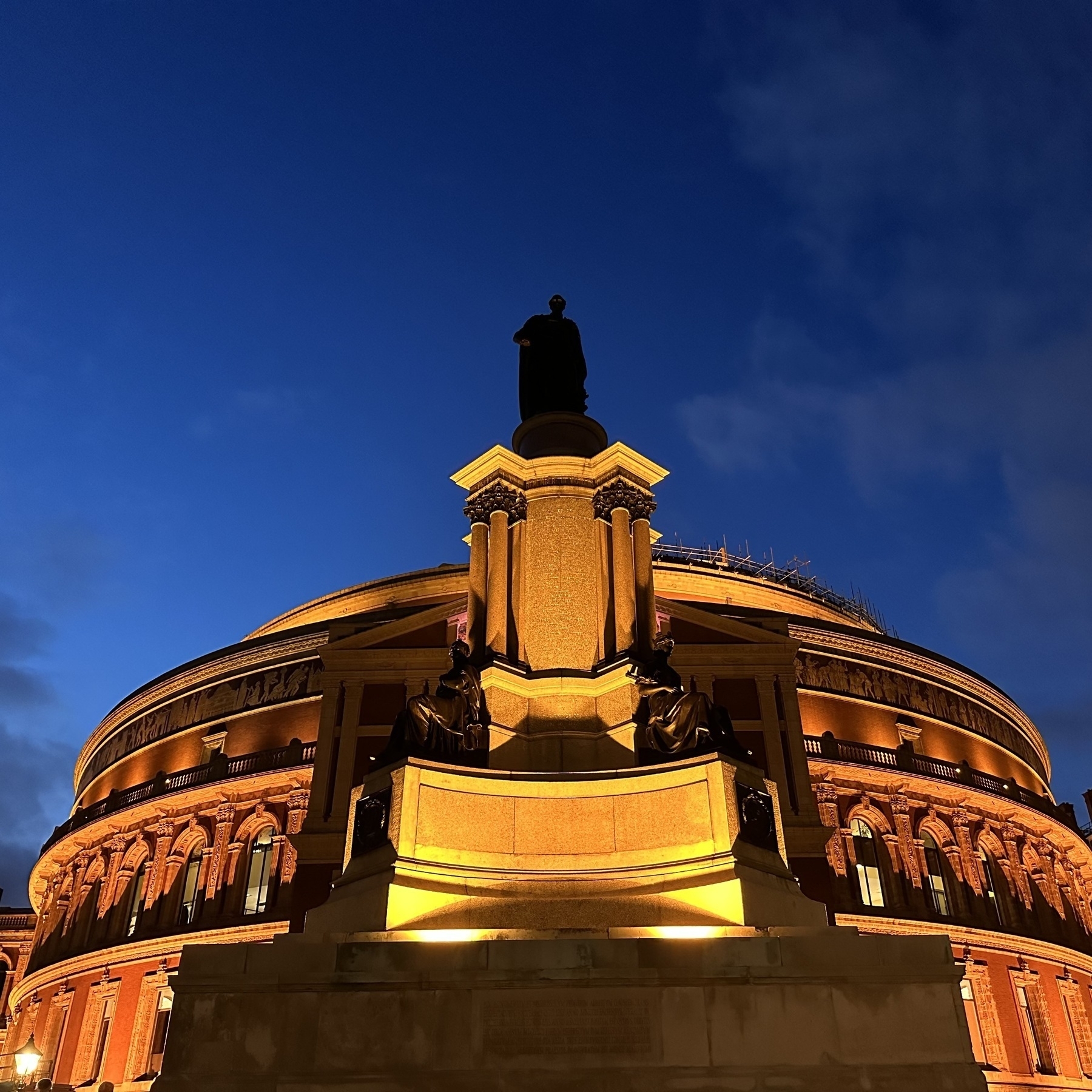 Silhouette of a statue against a dark blue sky at dusk, in front of the Royal Albert Hall.