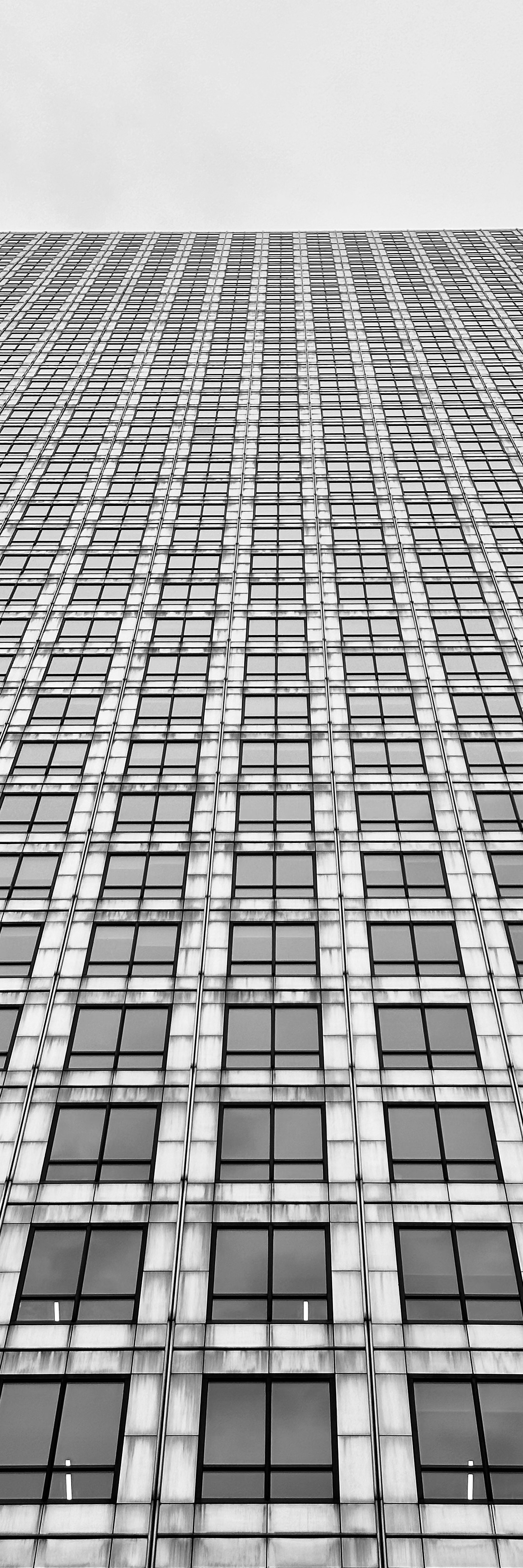 Black and white photo looking up at a skyscraper, soaring in to the sky.