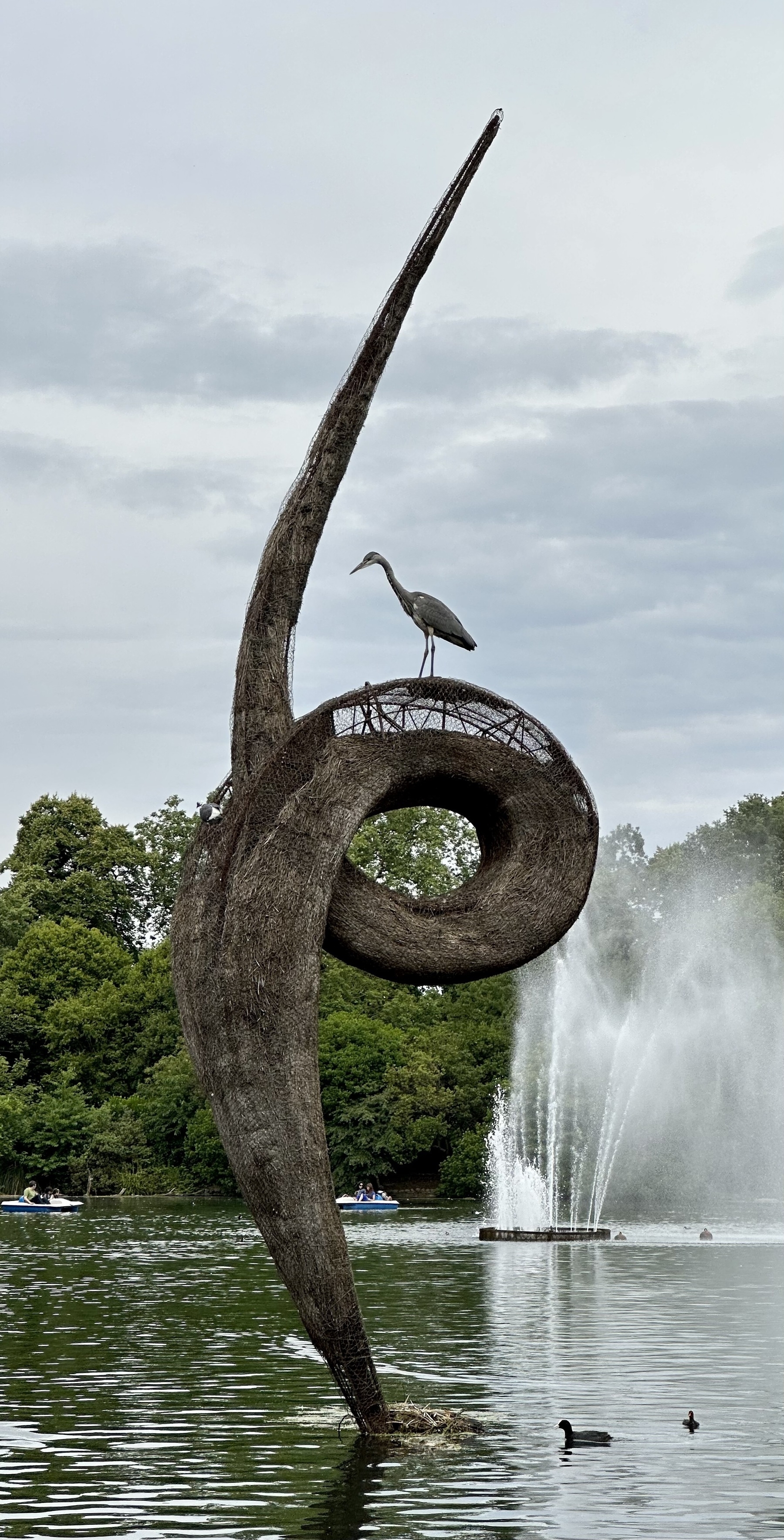 A heron perched on top of an abstract sculpture in a lake.