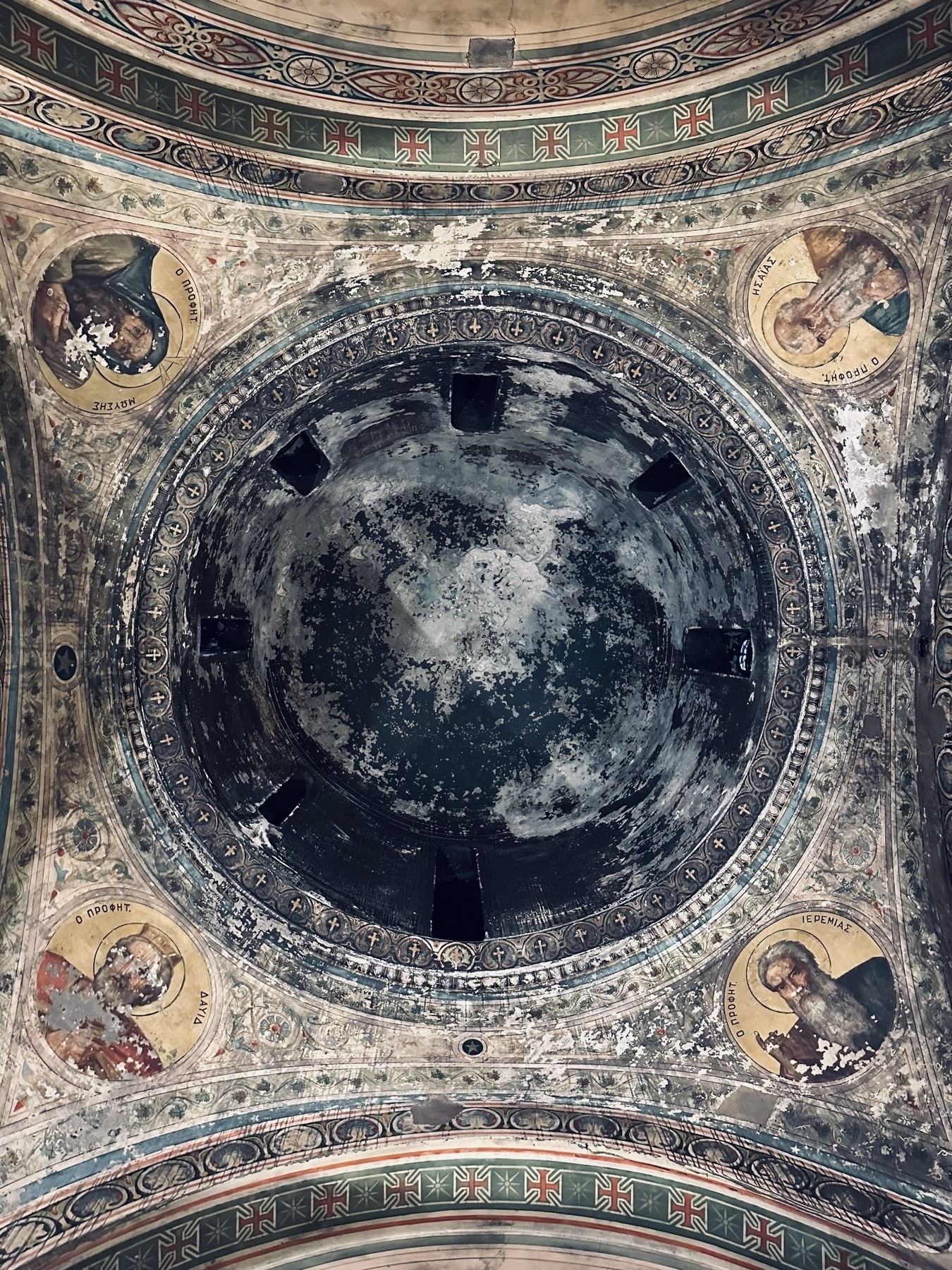 Looking directly up at the inside of a dome, painted dark but with flaking paint and religious paintings around the outside.