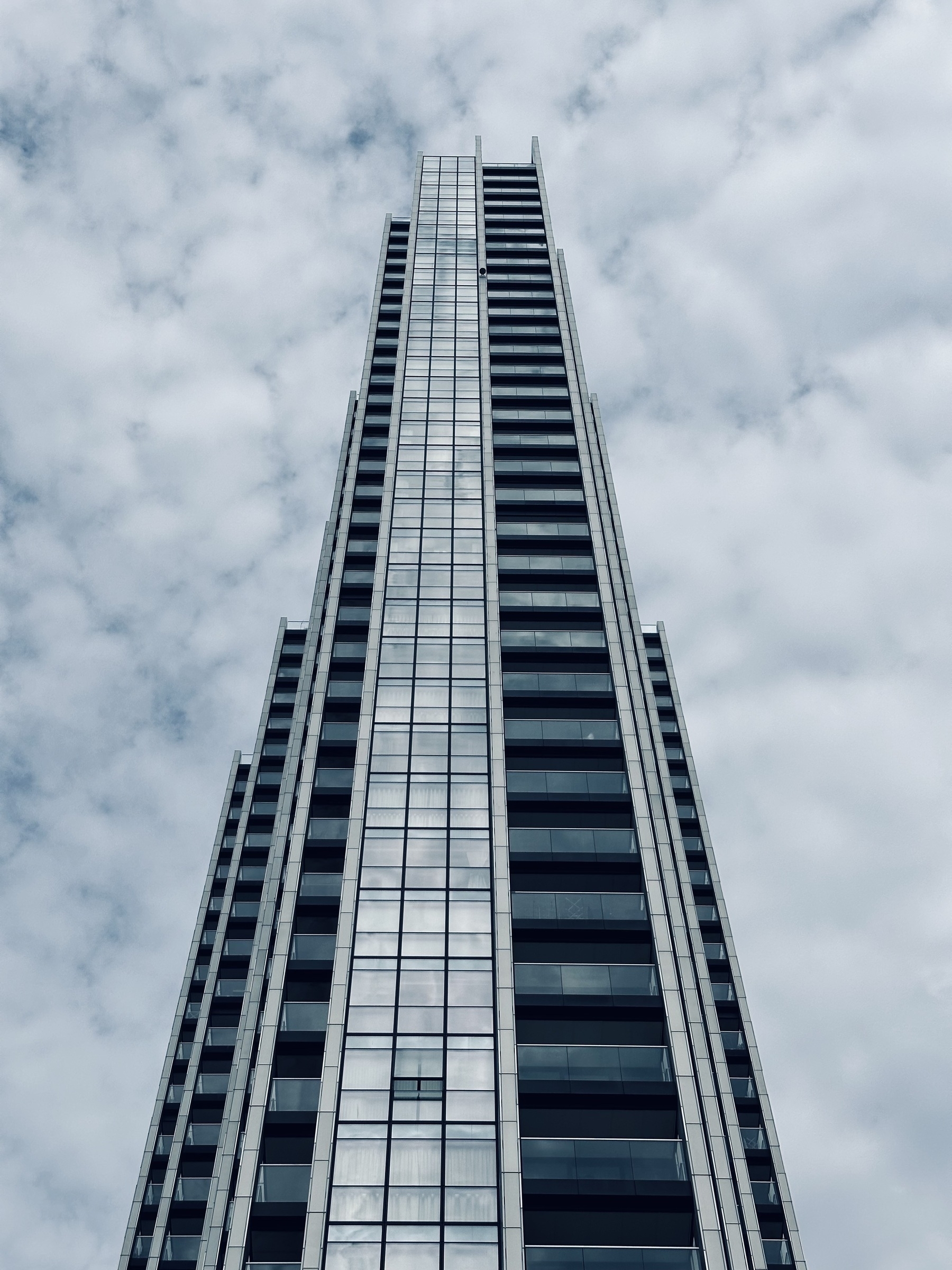 A tall building with balconies reaching up in to a cloudy sky.