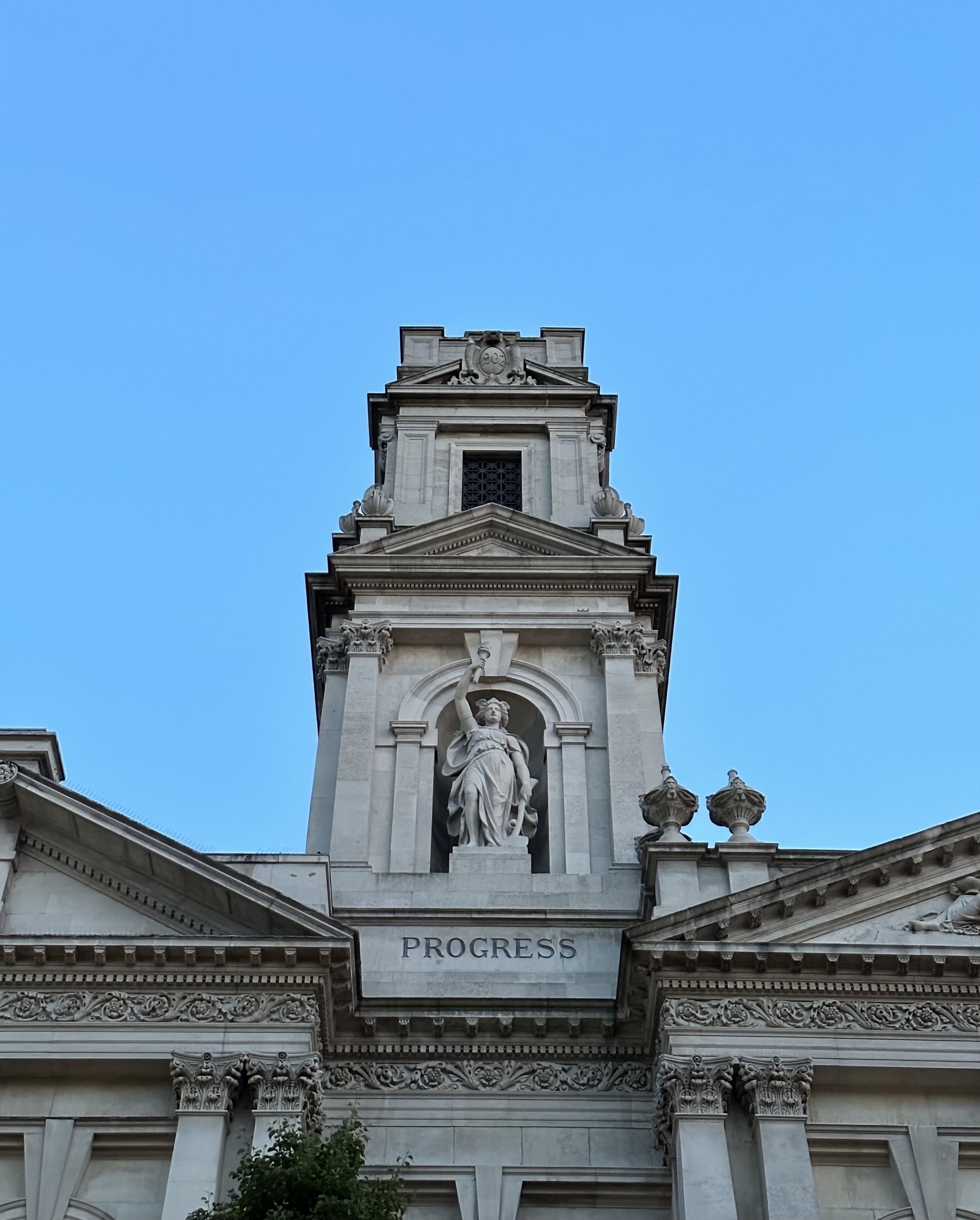 A stone building with a statue of a woman holding a torch and an axe, with the word progress underneath.