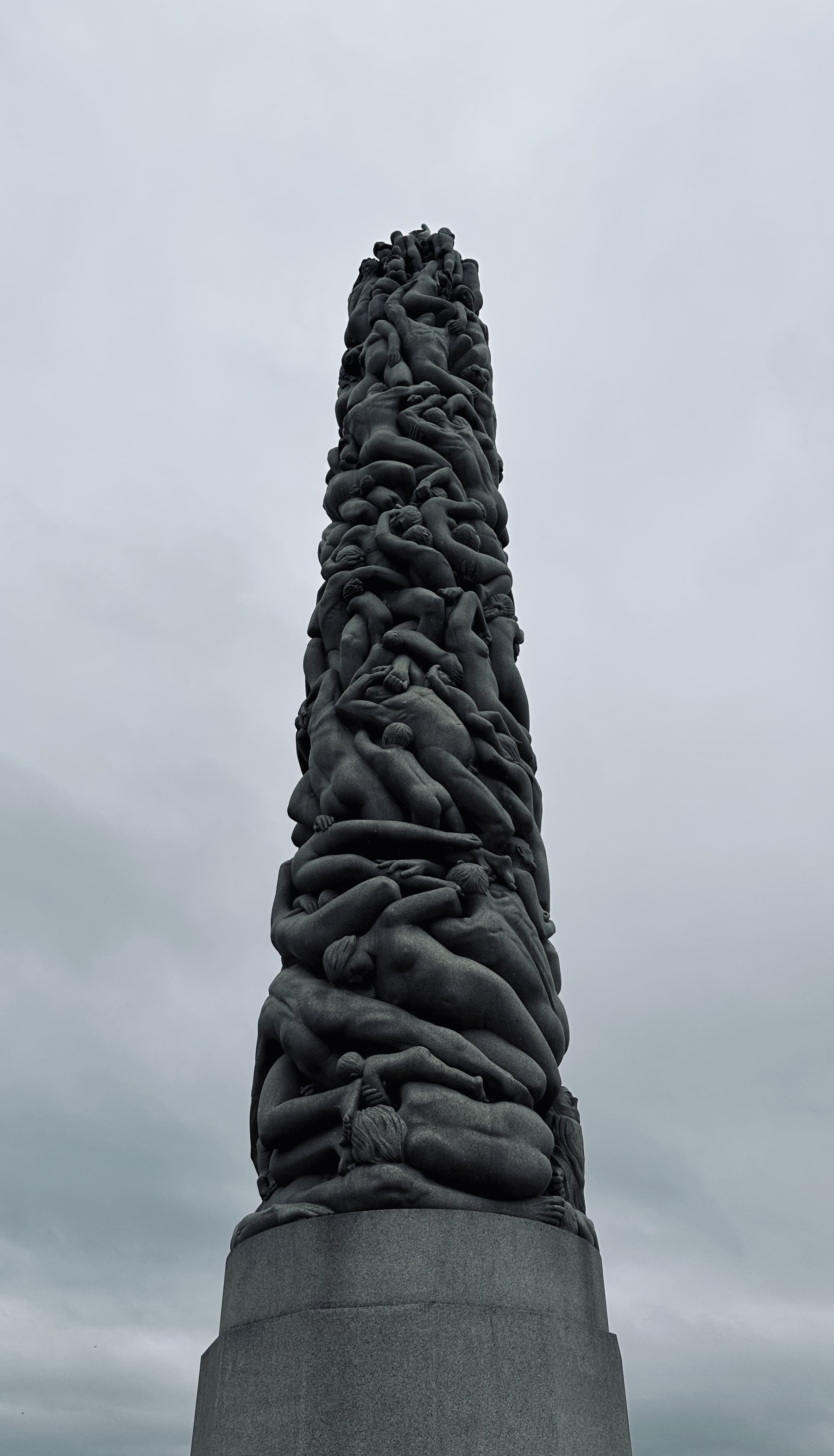 A carved stone pillar of nude figures against a grey sky.
