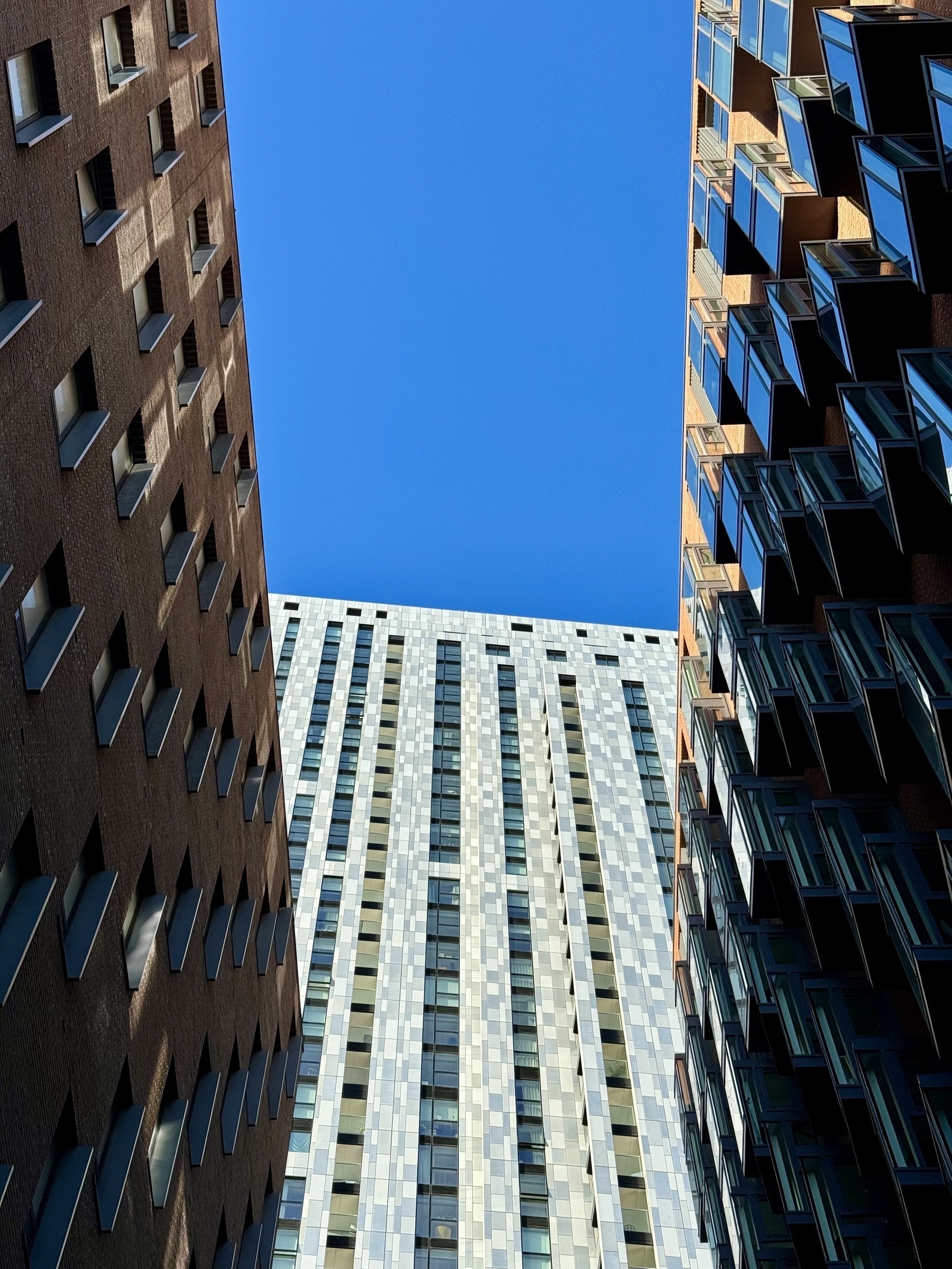 Looking up at three buildings forming a U-shape of bright blue sky.