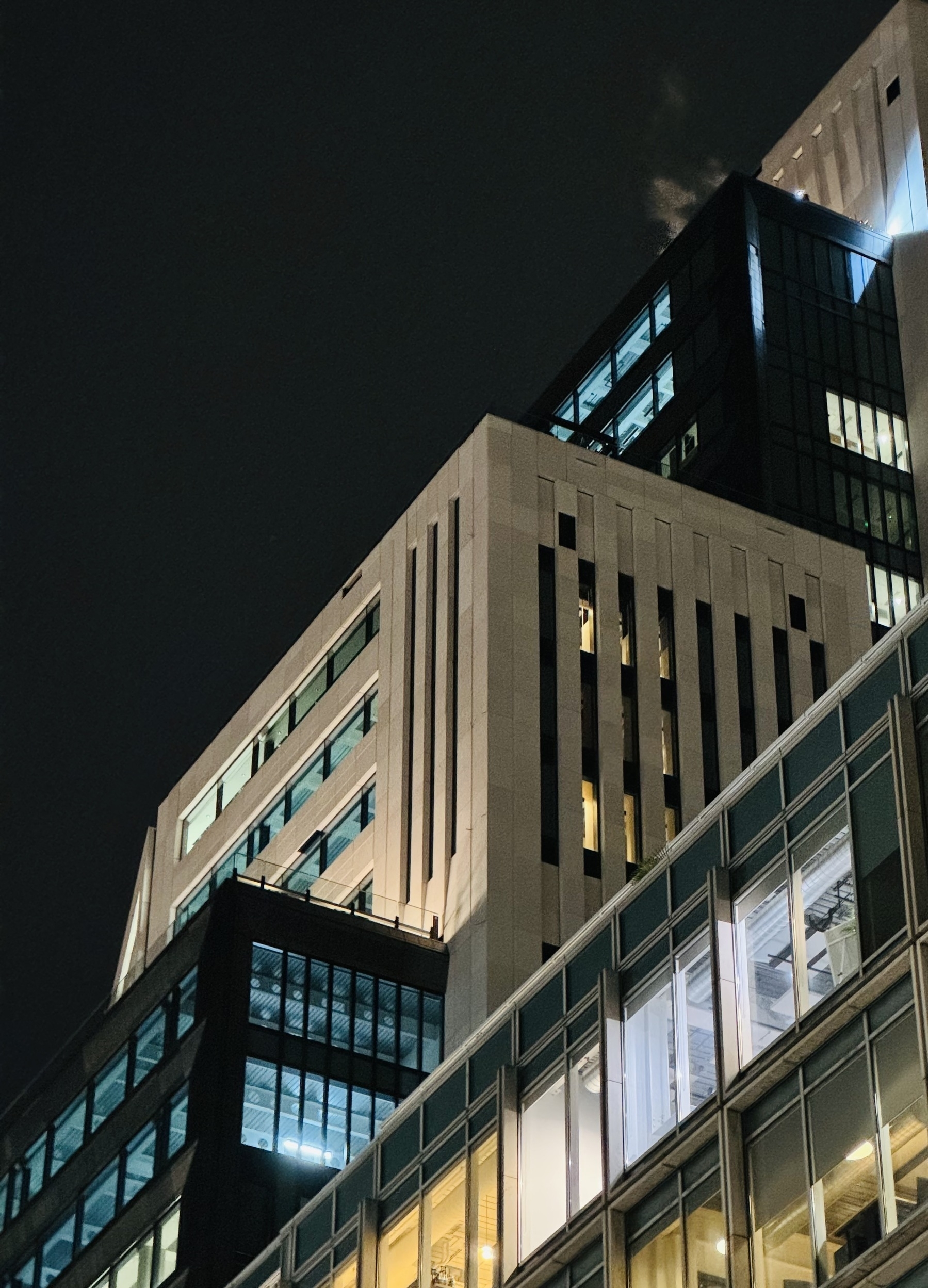 Looking up at a building at night, with alternating black and white segments stepping back as they rise.