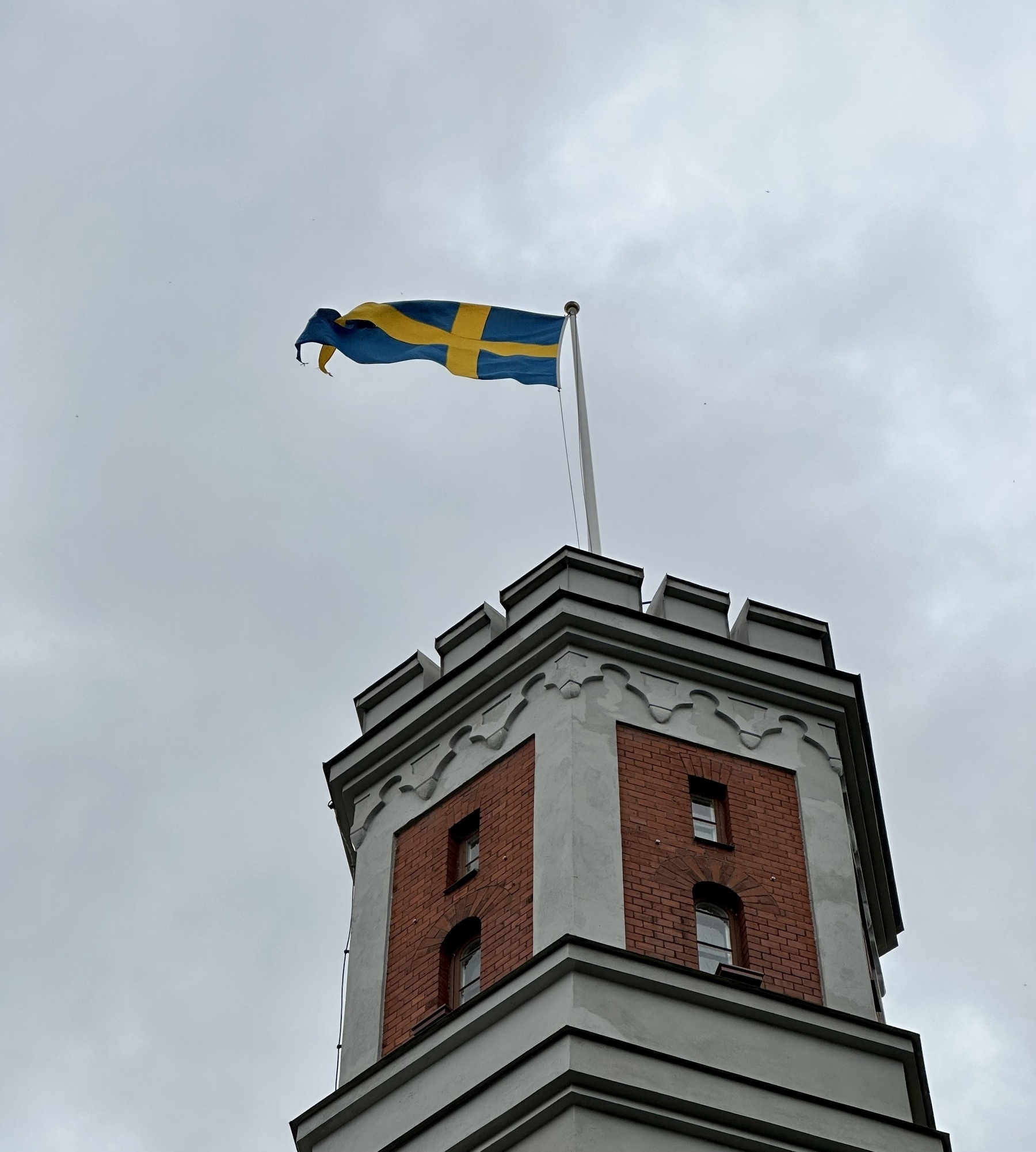 The Swedish flag flying from the top of a red brick and grey stone tower.