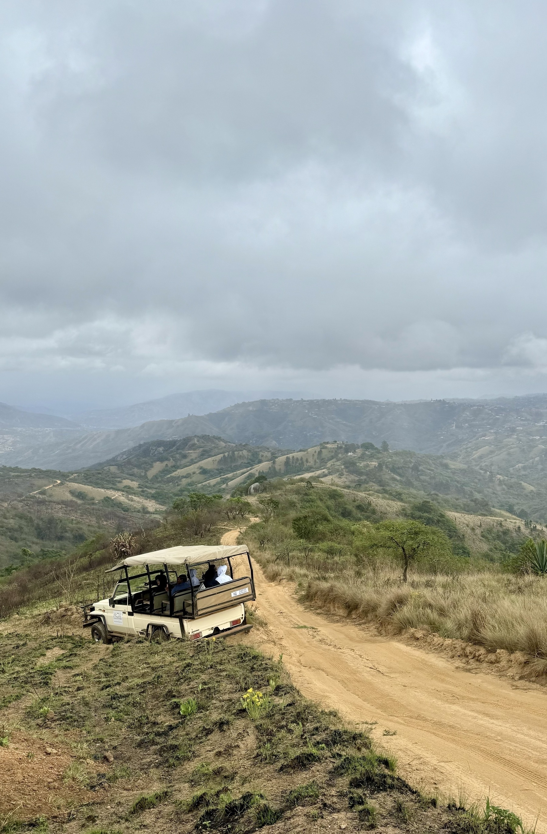 A jeep pulled over to the side of a dirt road that leads off into the hills, with clouds above.