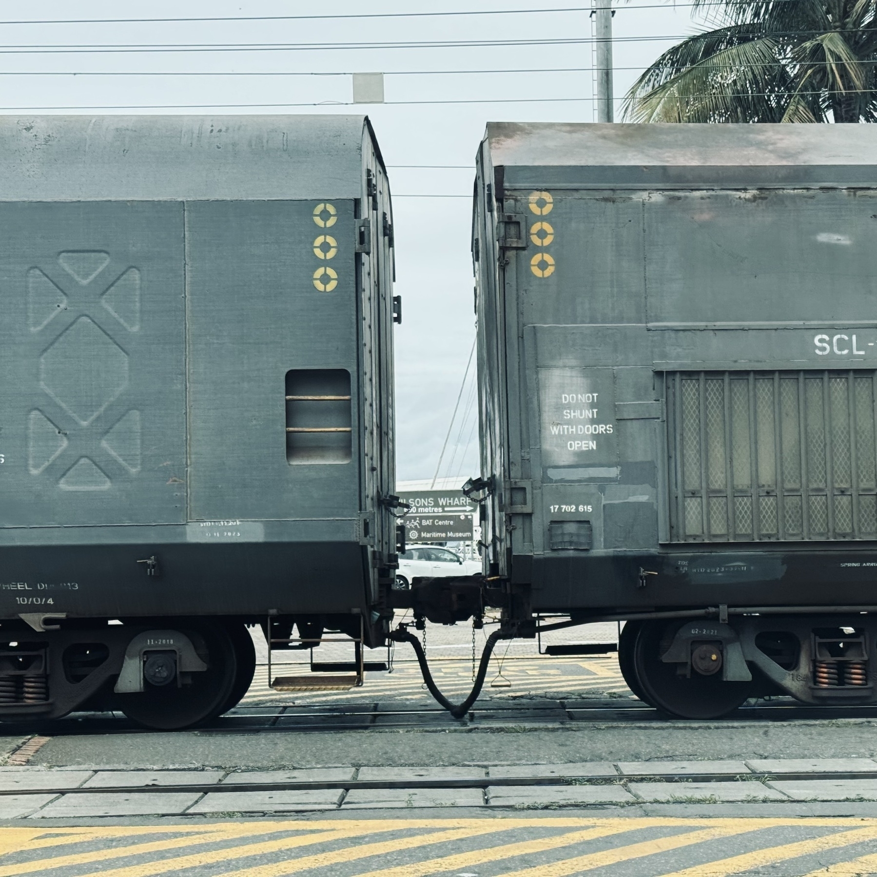 The ends of two covered train wagons on a level crossing, with a small gap between.