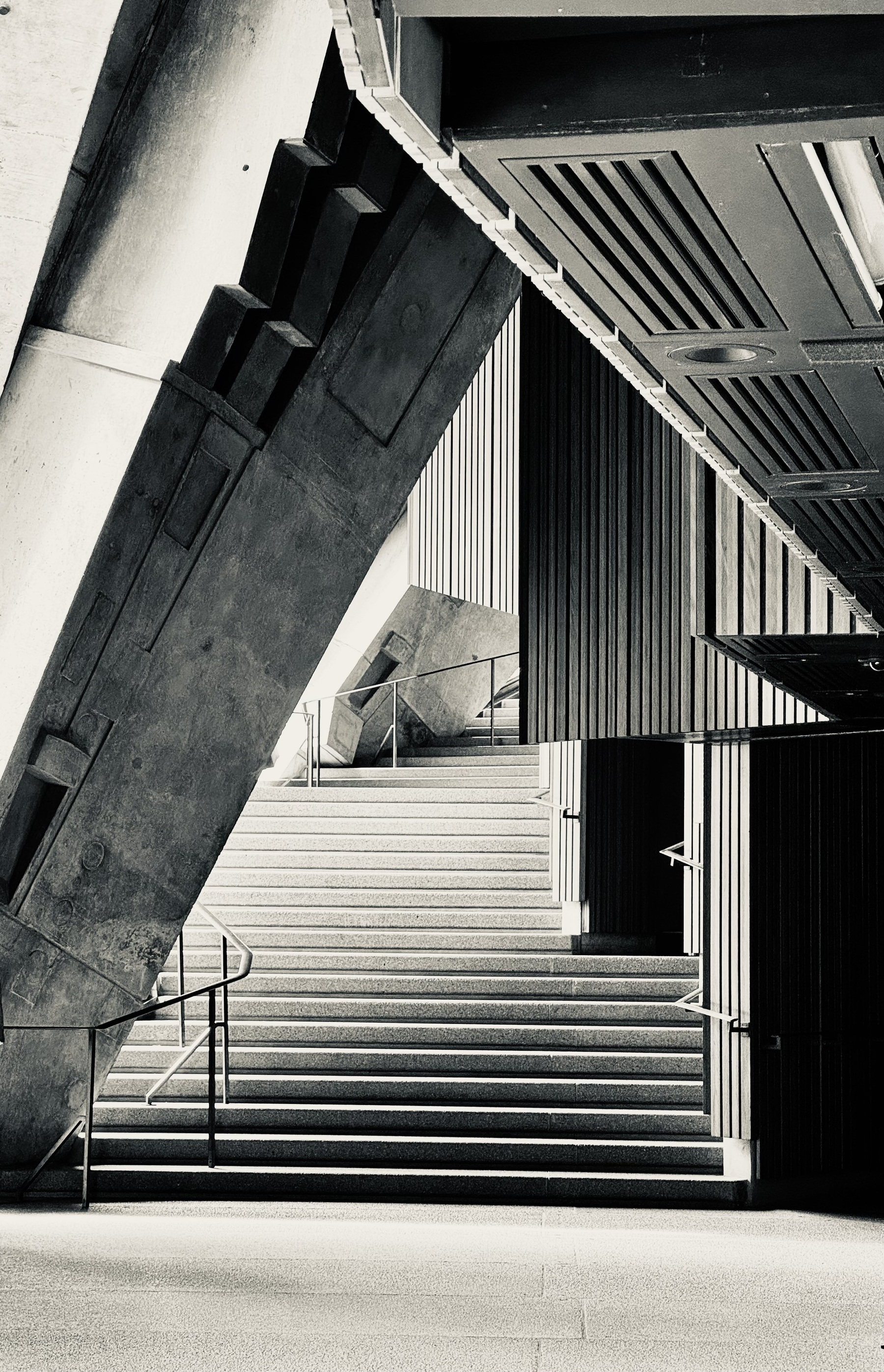 Black and white photo of concrete stairs with light on the left and wood panelling on the right, at Sydney Opera House.