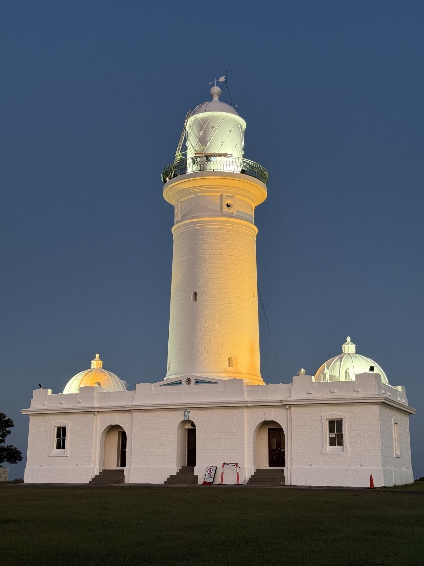 A white lighthouse with a rectangular building at the base, against a dark blue sky.