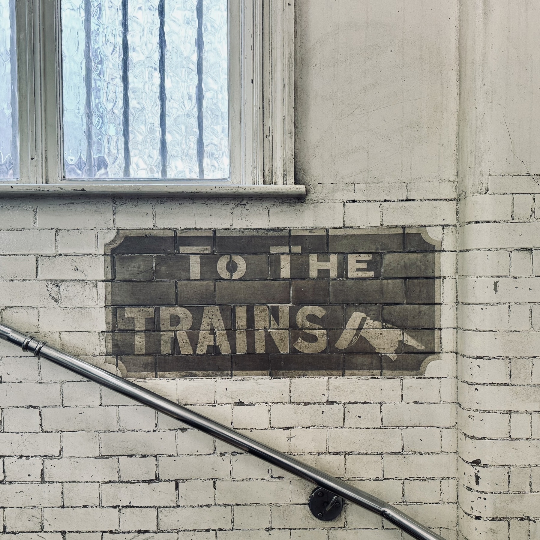 A sign painted on brickwork that says “to the trains”.