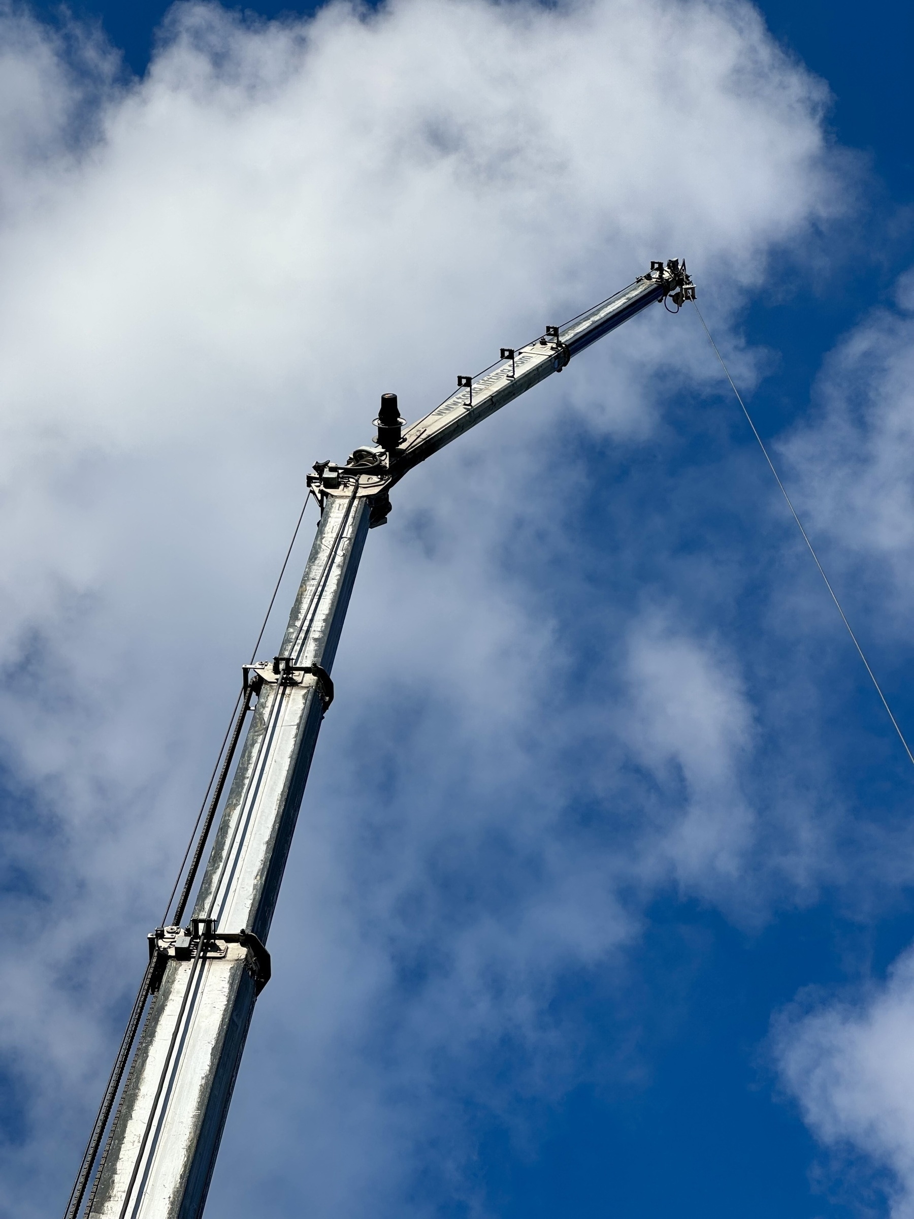 A mobile crane reaching in to a white and blue sky.