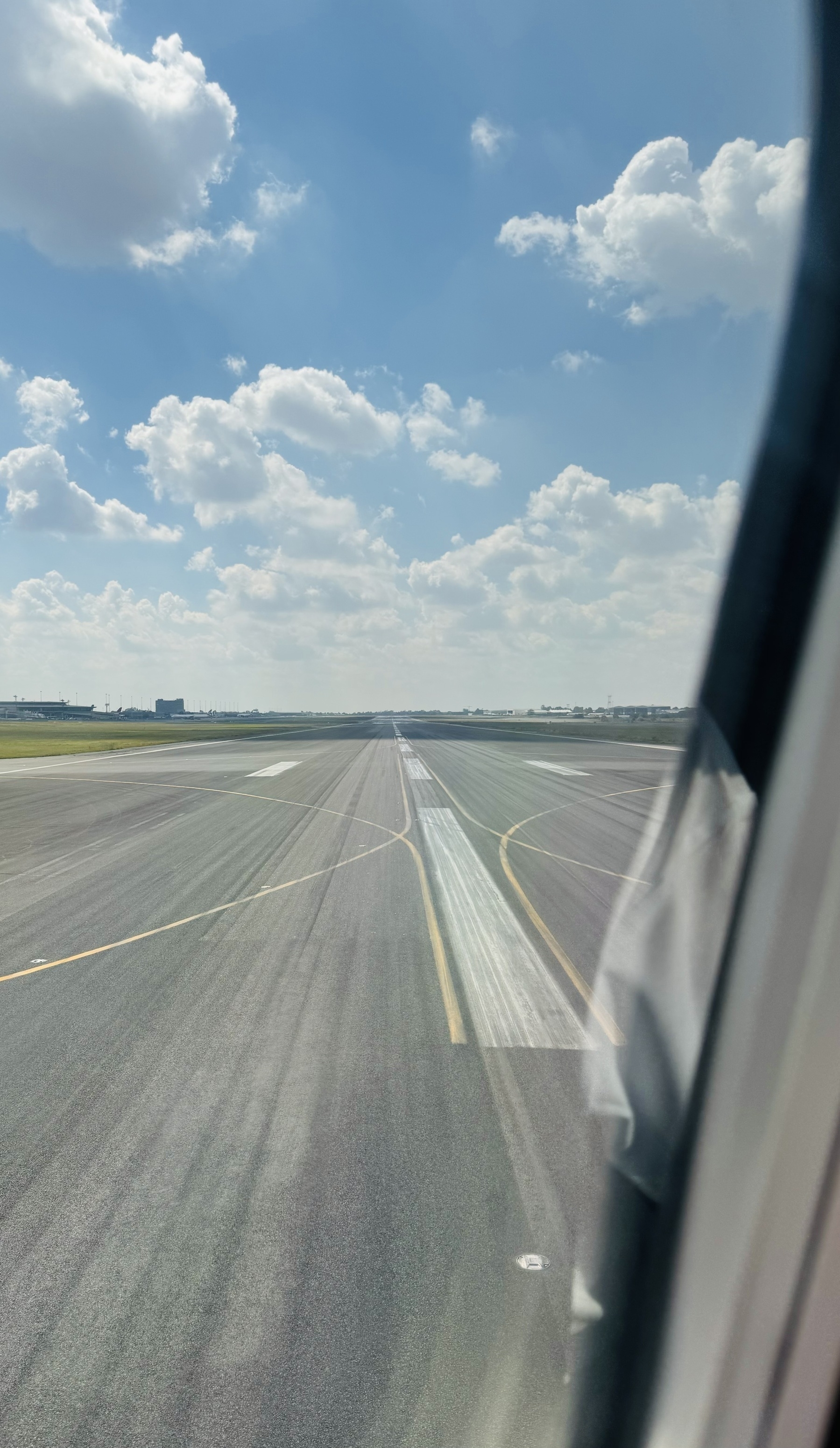 Looking out the window of a plane as it turns on to the runway in Johannesburg to take off. It’s sunny, with white clouds in a blue sky.