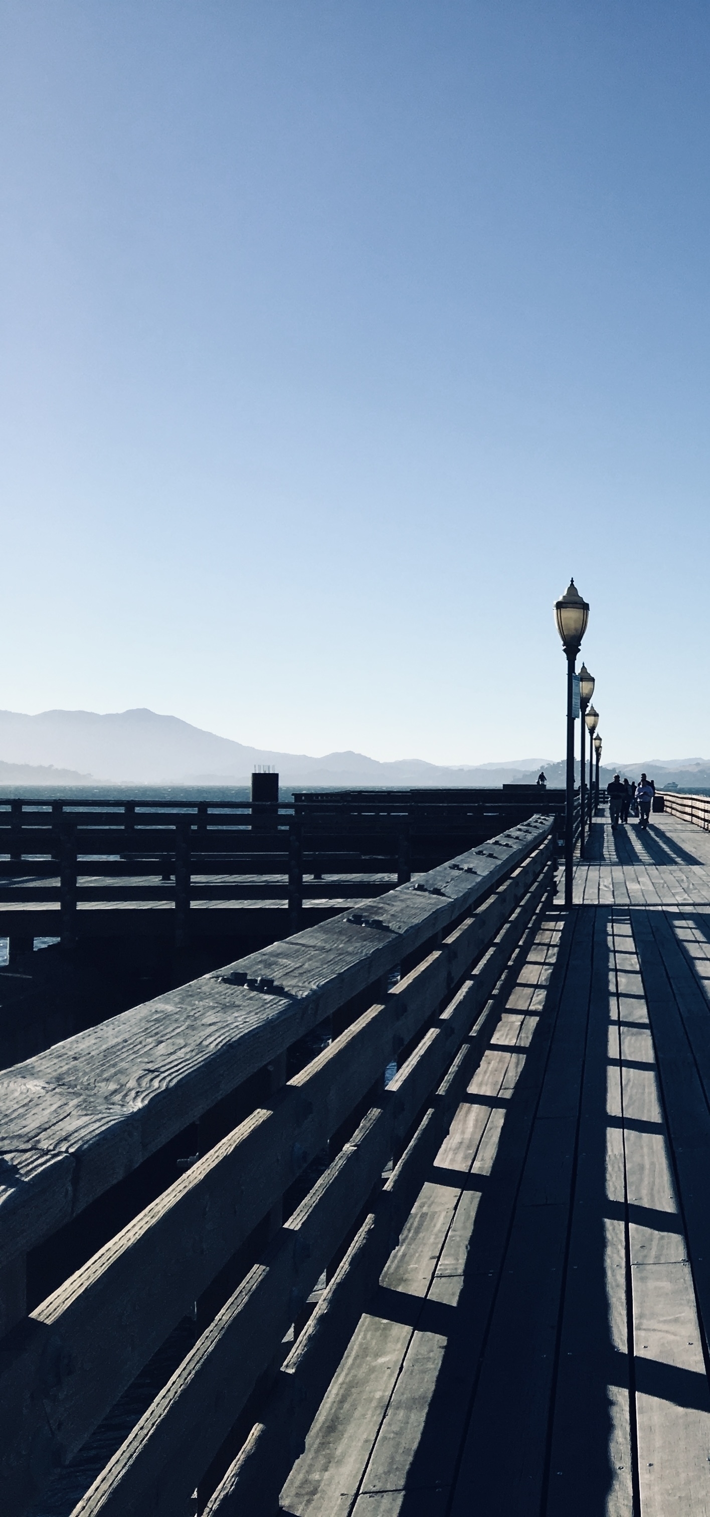 A wooden pier with lamps, and hills visible through the haze on the horizon.