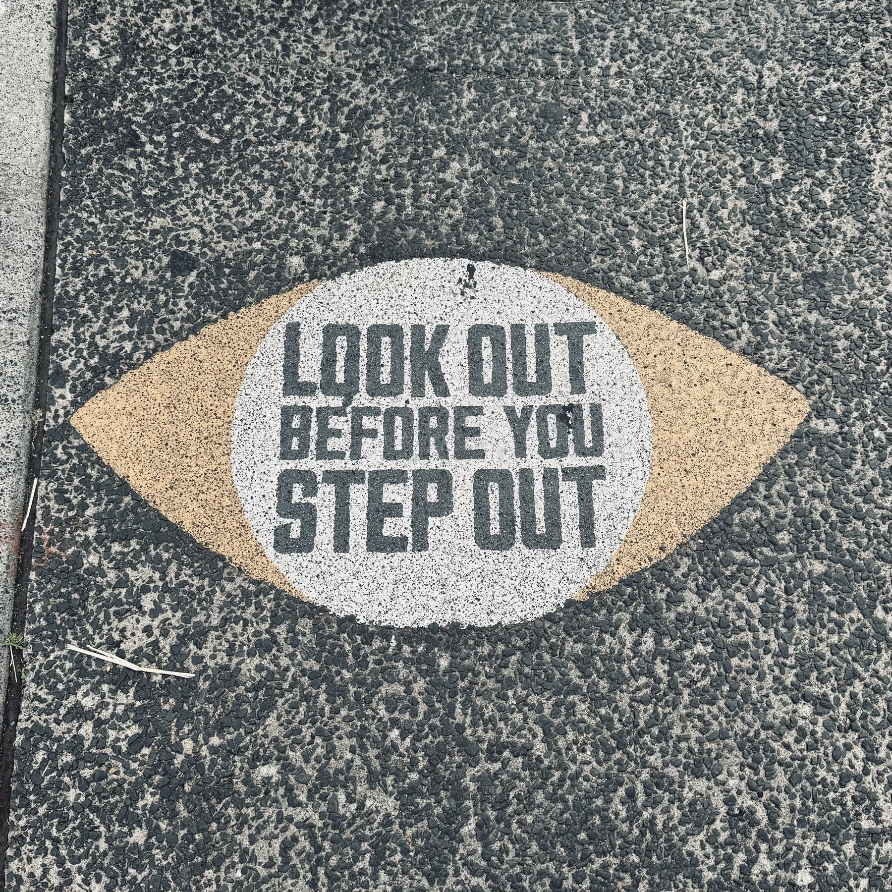 A warning that says “Look out before you step out” on the pavement by a crossing.