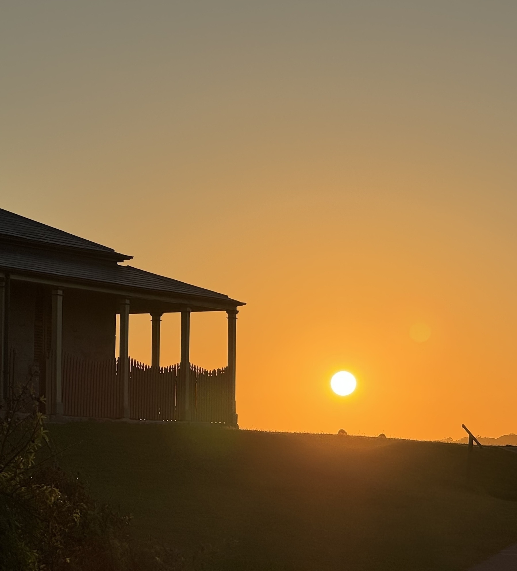 The sun setting next to a lighthouse keeper’s cottage with a veranda around the outside.