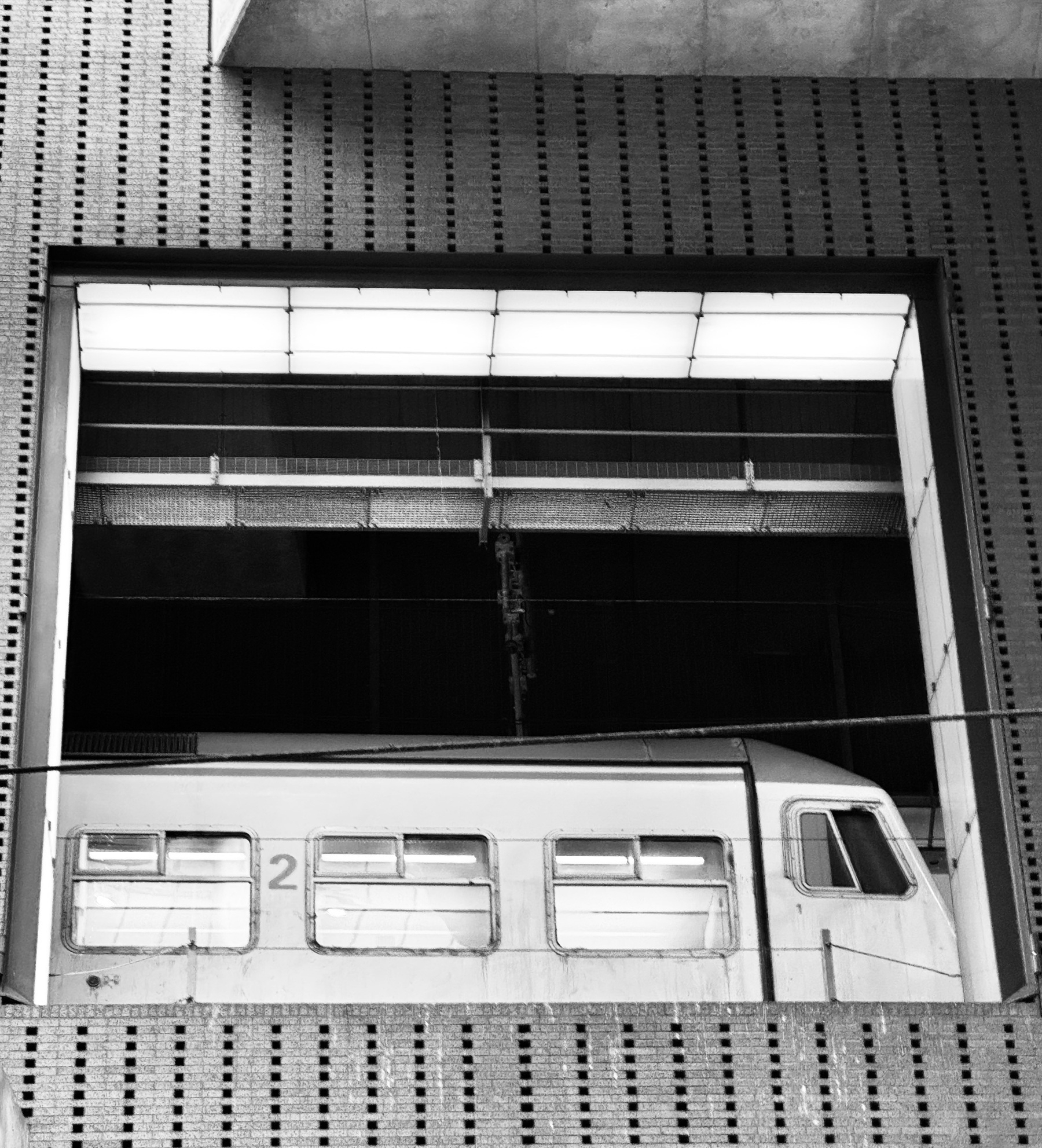 Train windows seen through a large opening in a brick wall.
