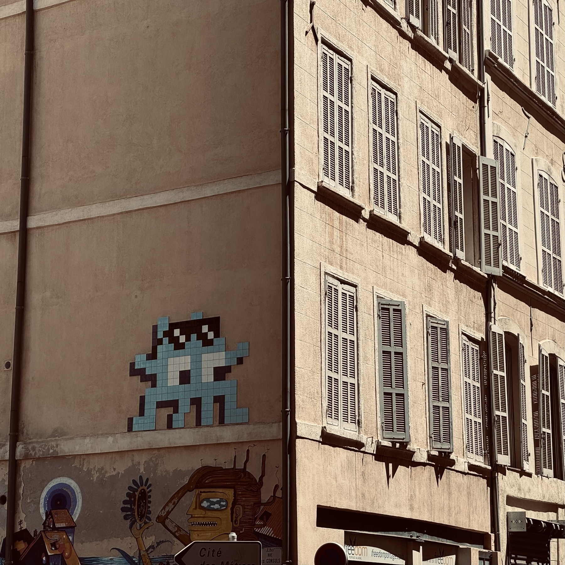 Pixel art on the shady side of a building, with the other face of the building in the sunlight.