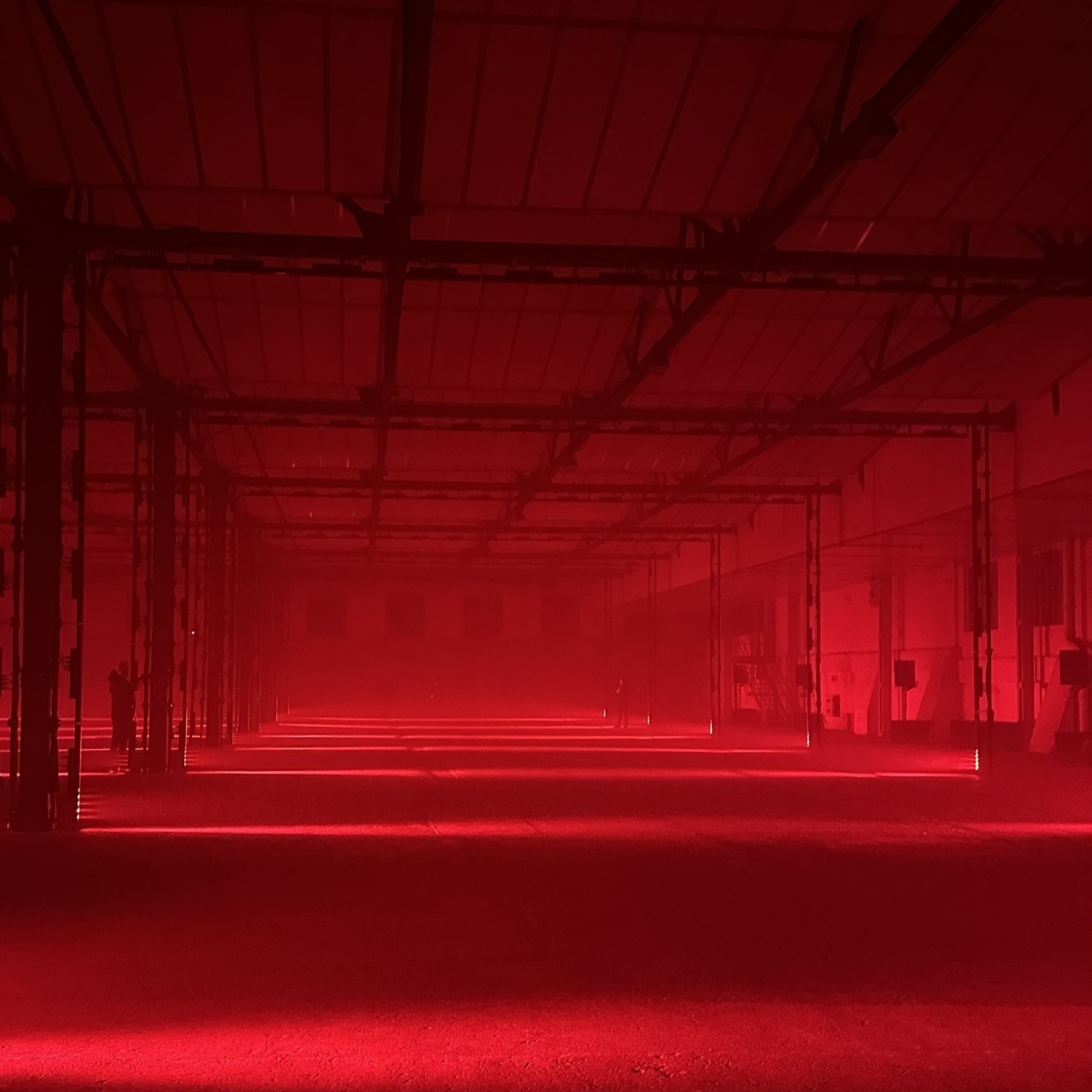 An empty warehouse with haze in the distance, lit with red light.