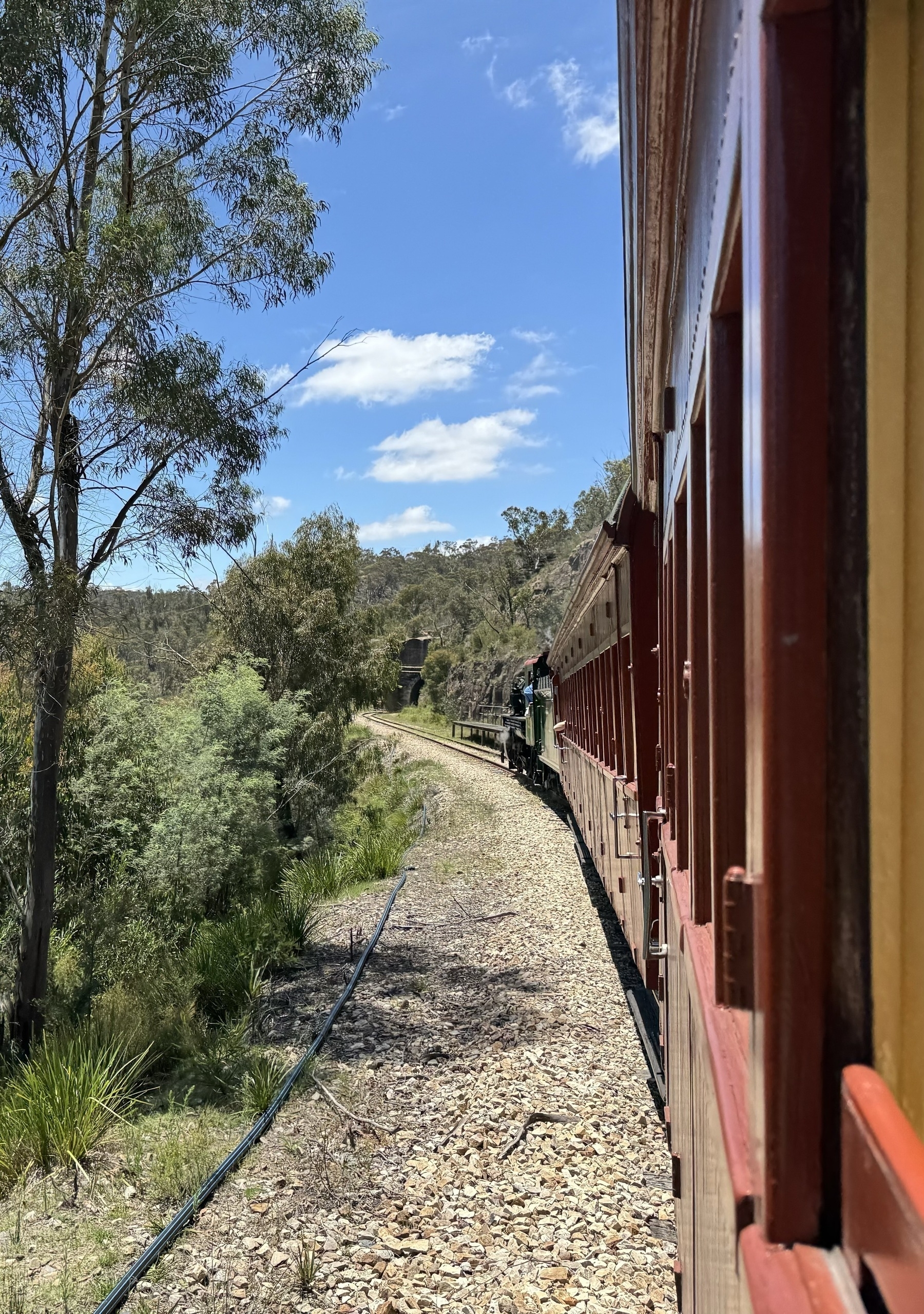 Looking along the side of a train towards the steam locomotive at the front. In the distance is the entrance to a tunnel.