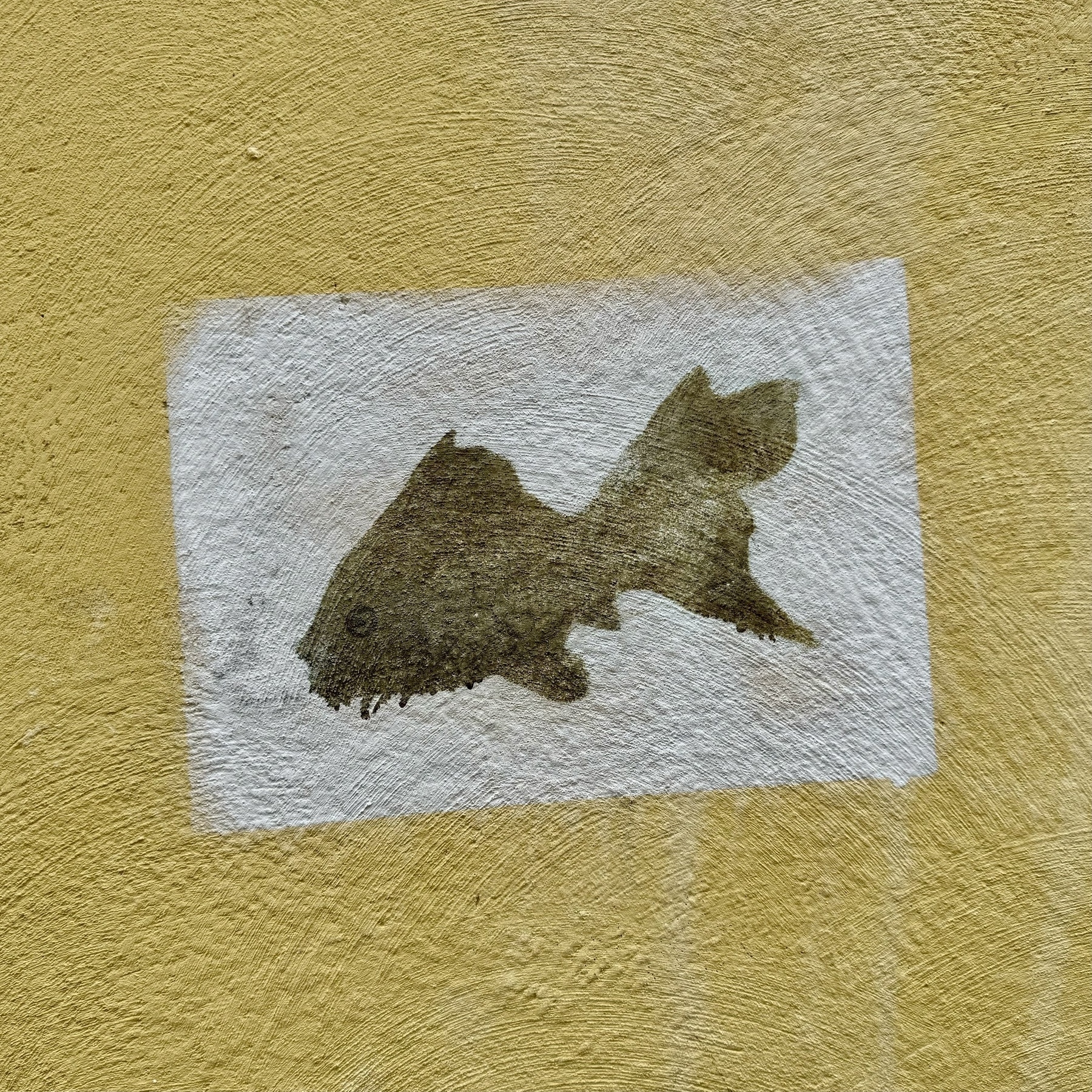 A graffiti fish painted on a white rectangle on a yellow wall.