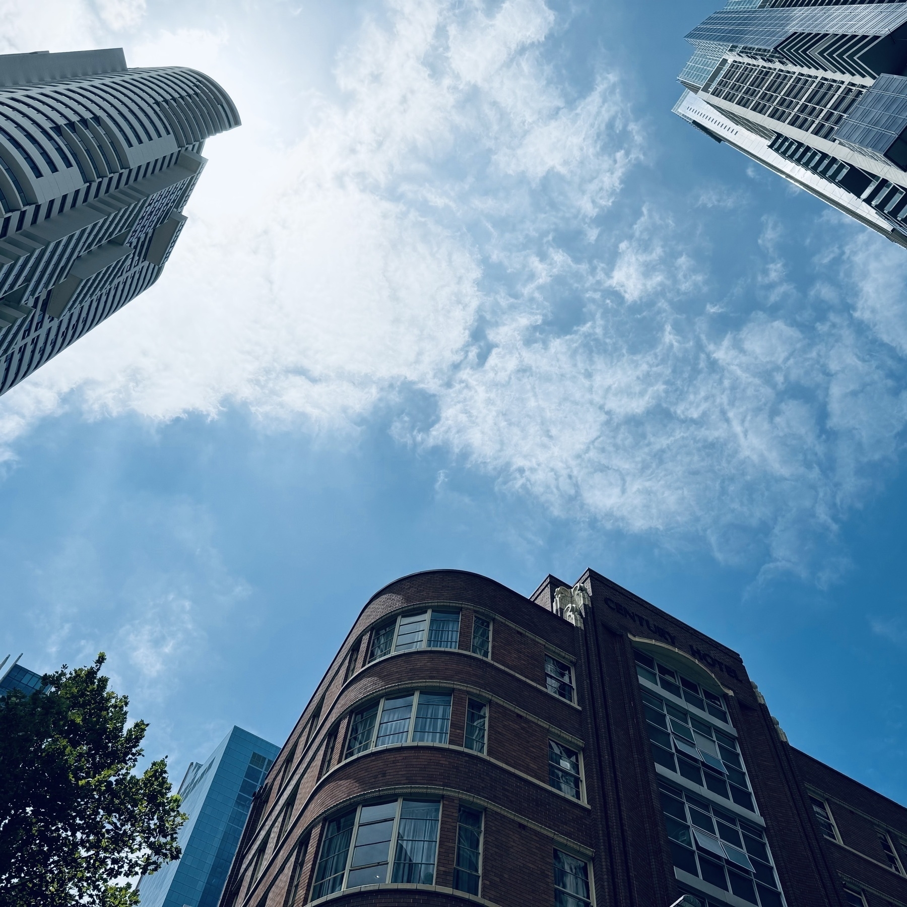 Looking up at a blue sky with white clouds, while three buildings protrude in from the edges of the photo.