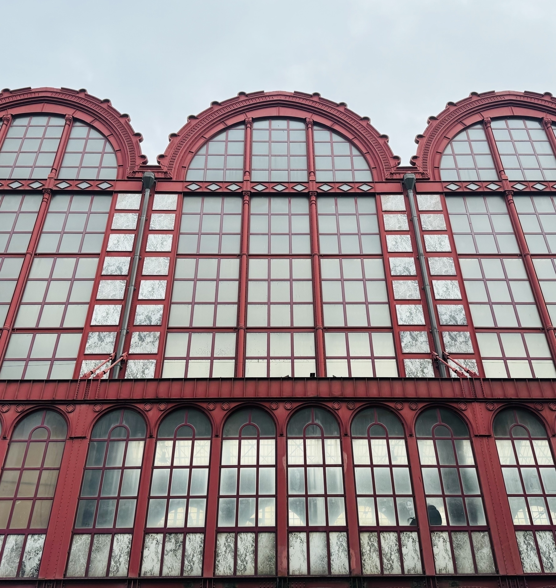 Red metalwork arching in to the sky holding glass panes, at Antwerp train station.
