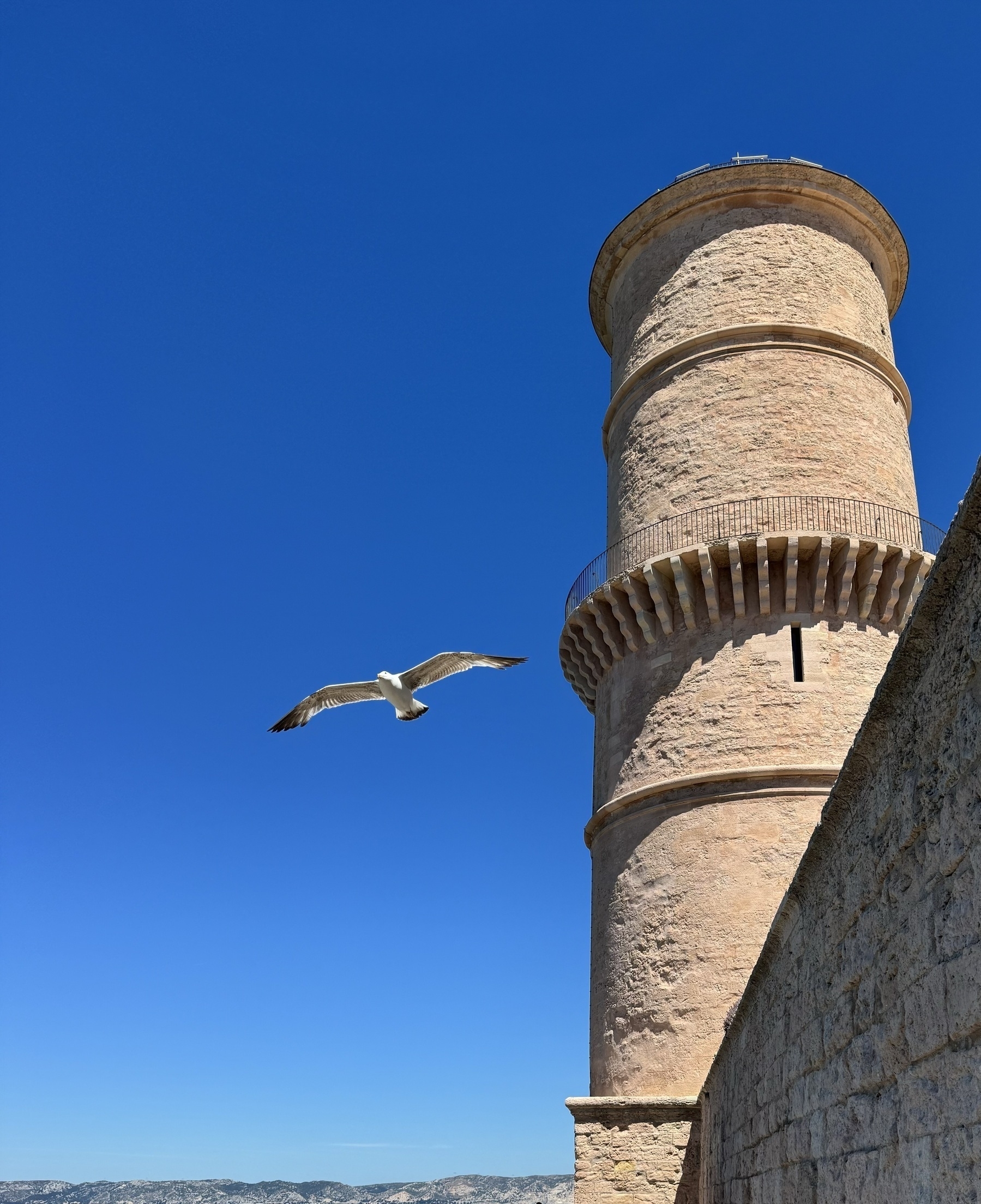 A seagull flying next to a stone tower, with a flawless blue sky in the background.