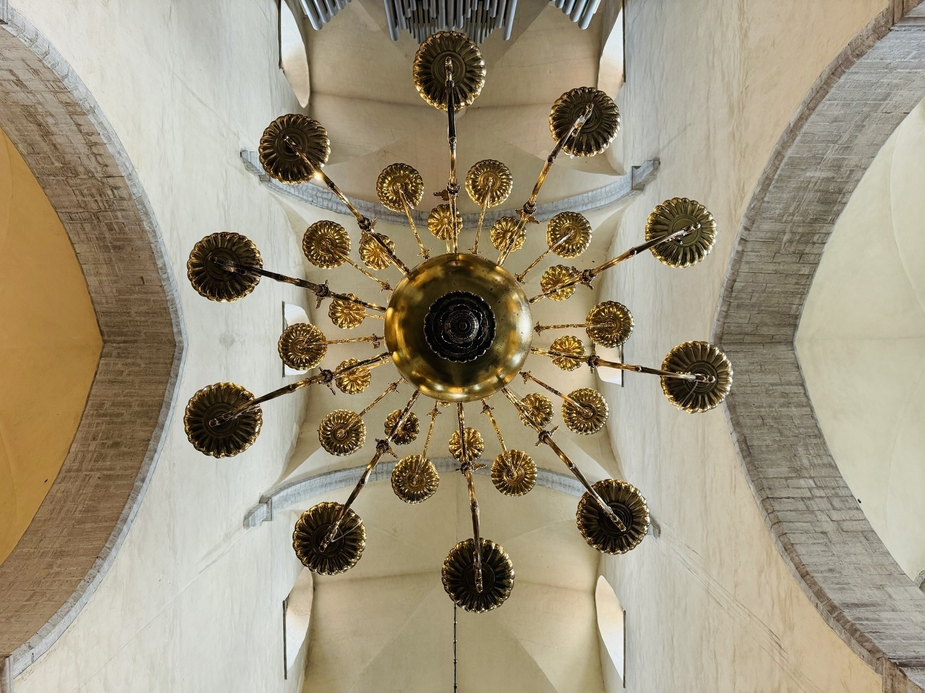 Looking up at the bottom of a golden chandelier that’s hanging from the vault of a church.