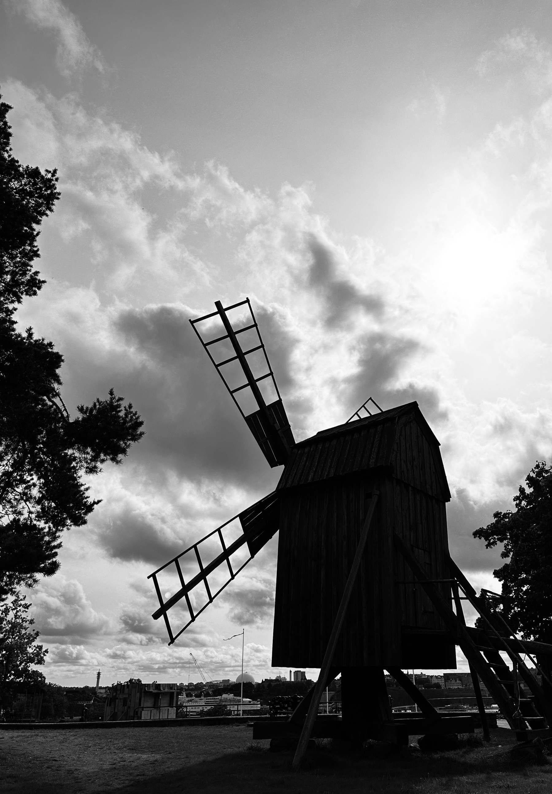 A windmill in silhouette against a cloudy sky, with trees to the left and right.