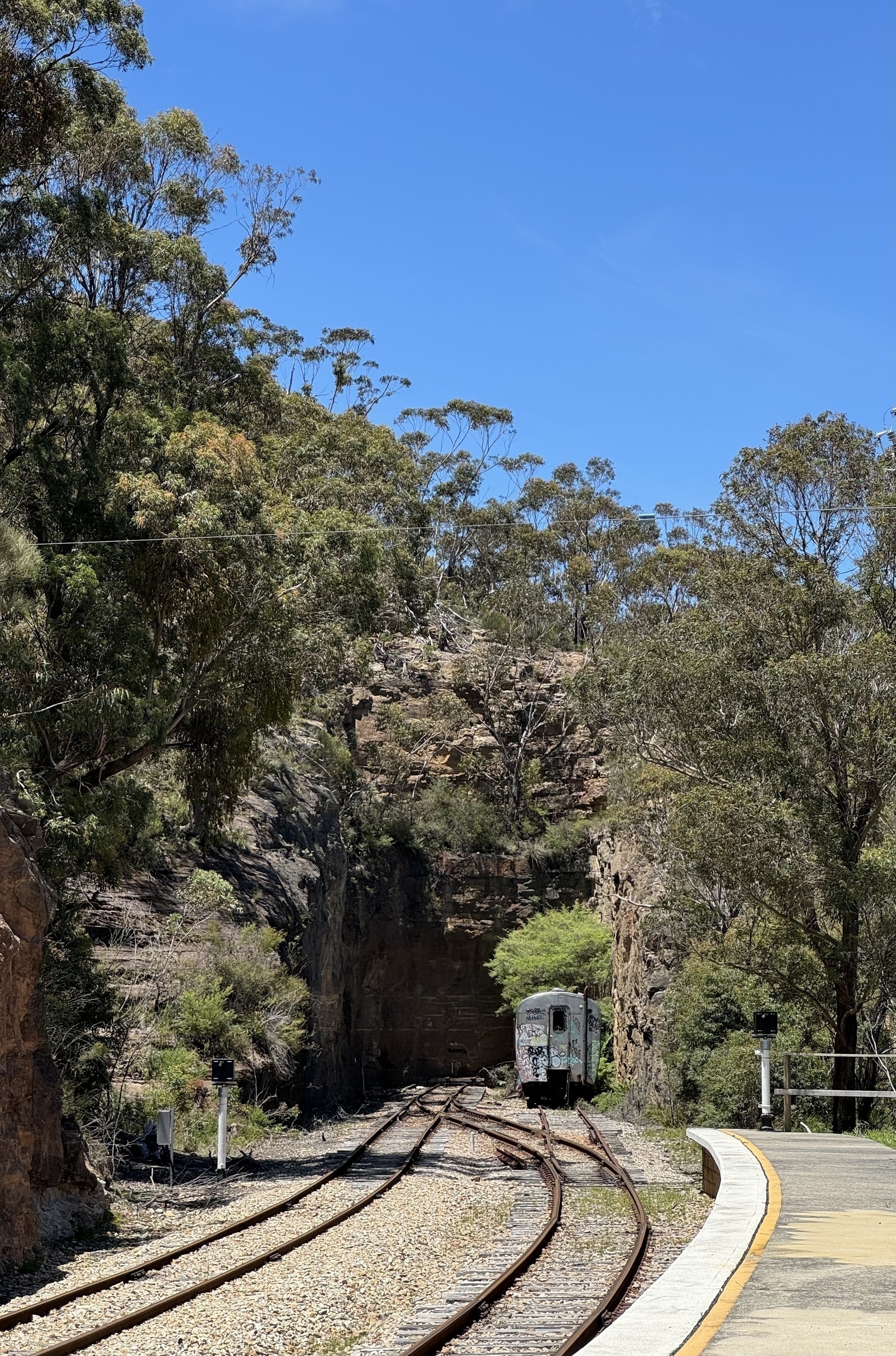 An old train carriage at the end of a train line that finishes by a rock face.