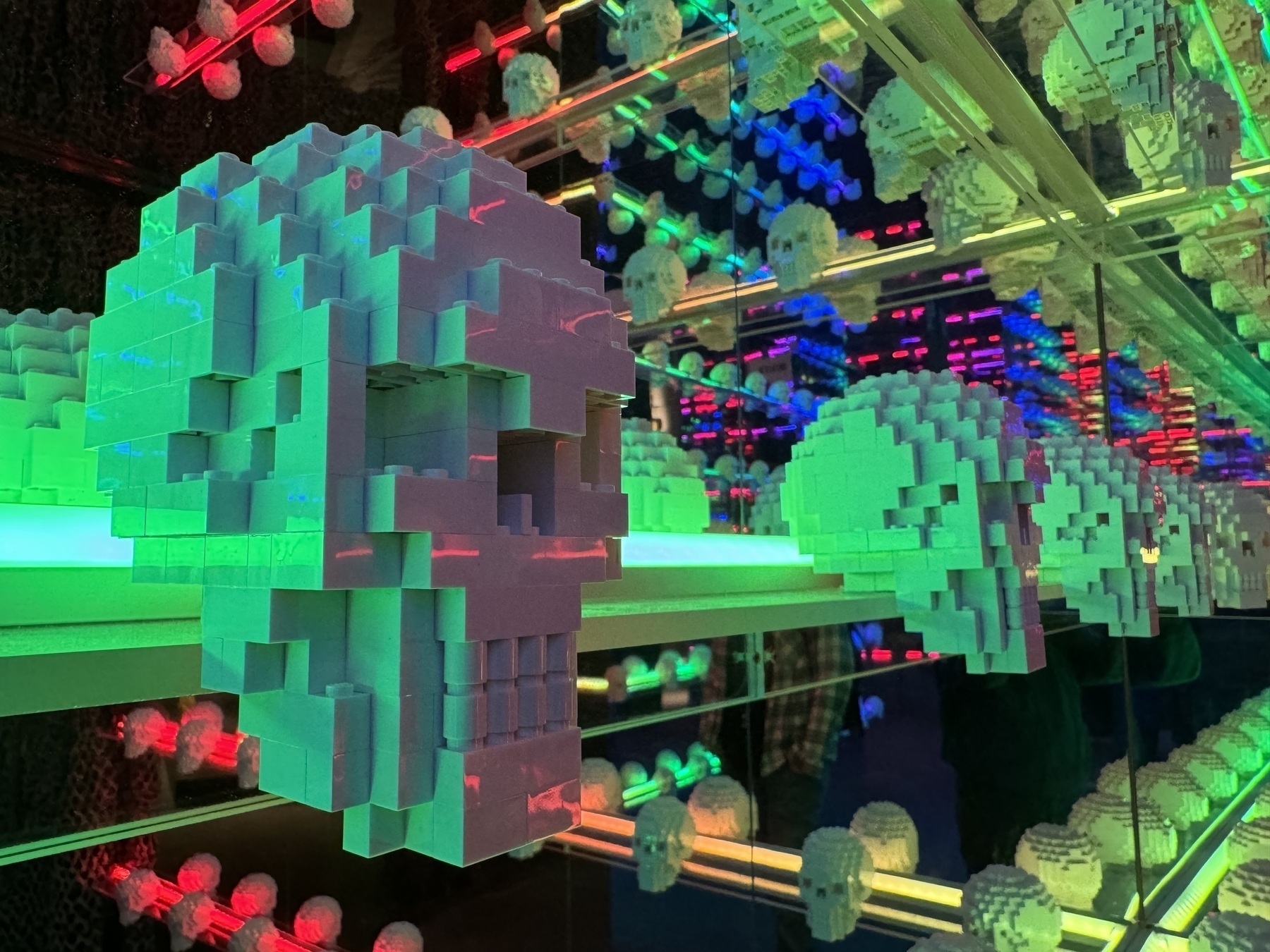 Colourfully lit Lego skulls in a mirrored room, reflecting in to the distance.