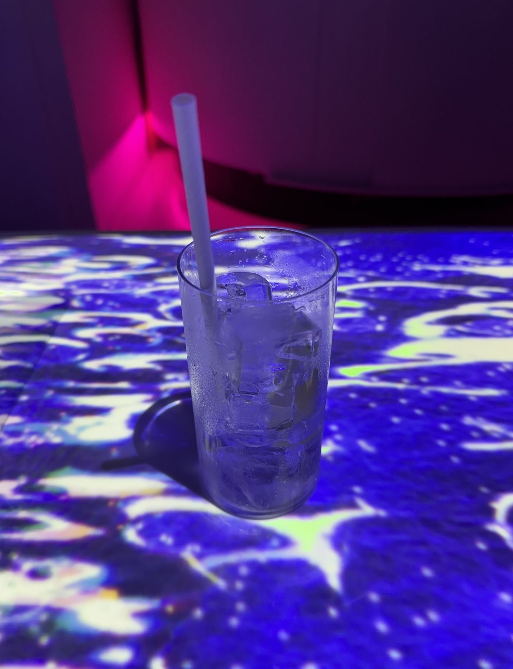 A lychee mocktail sitting on a table that’s got swirling blue patterns projected on it from above.