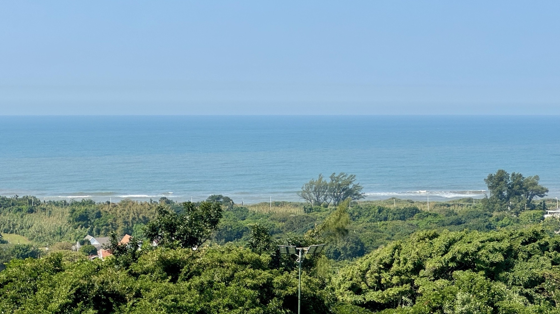 A view of the ocean with blue sky above and green trees below.