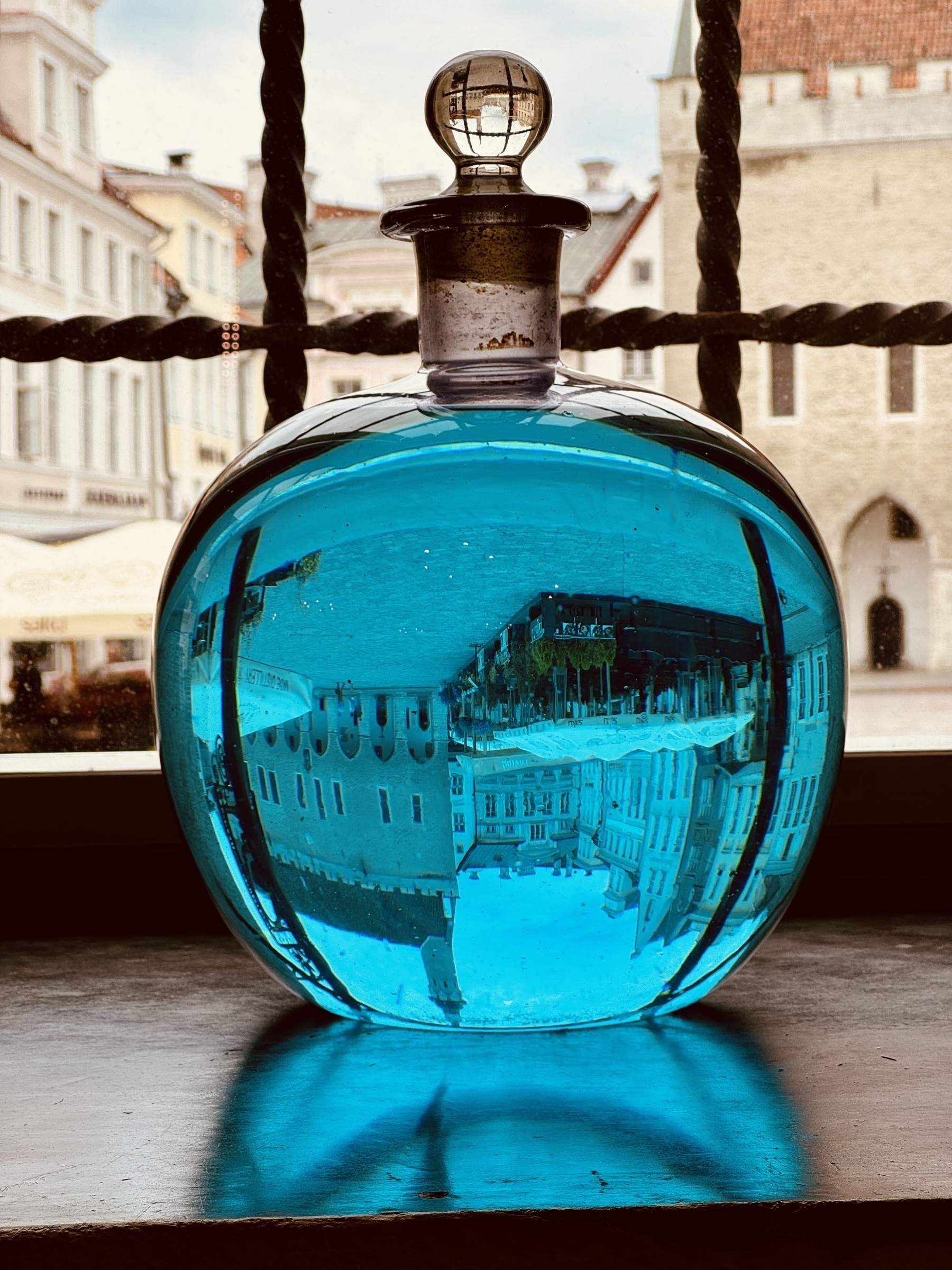 The main square of Tallinn seen upside down through a round bottle of blue liquid.