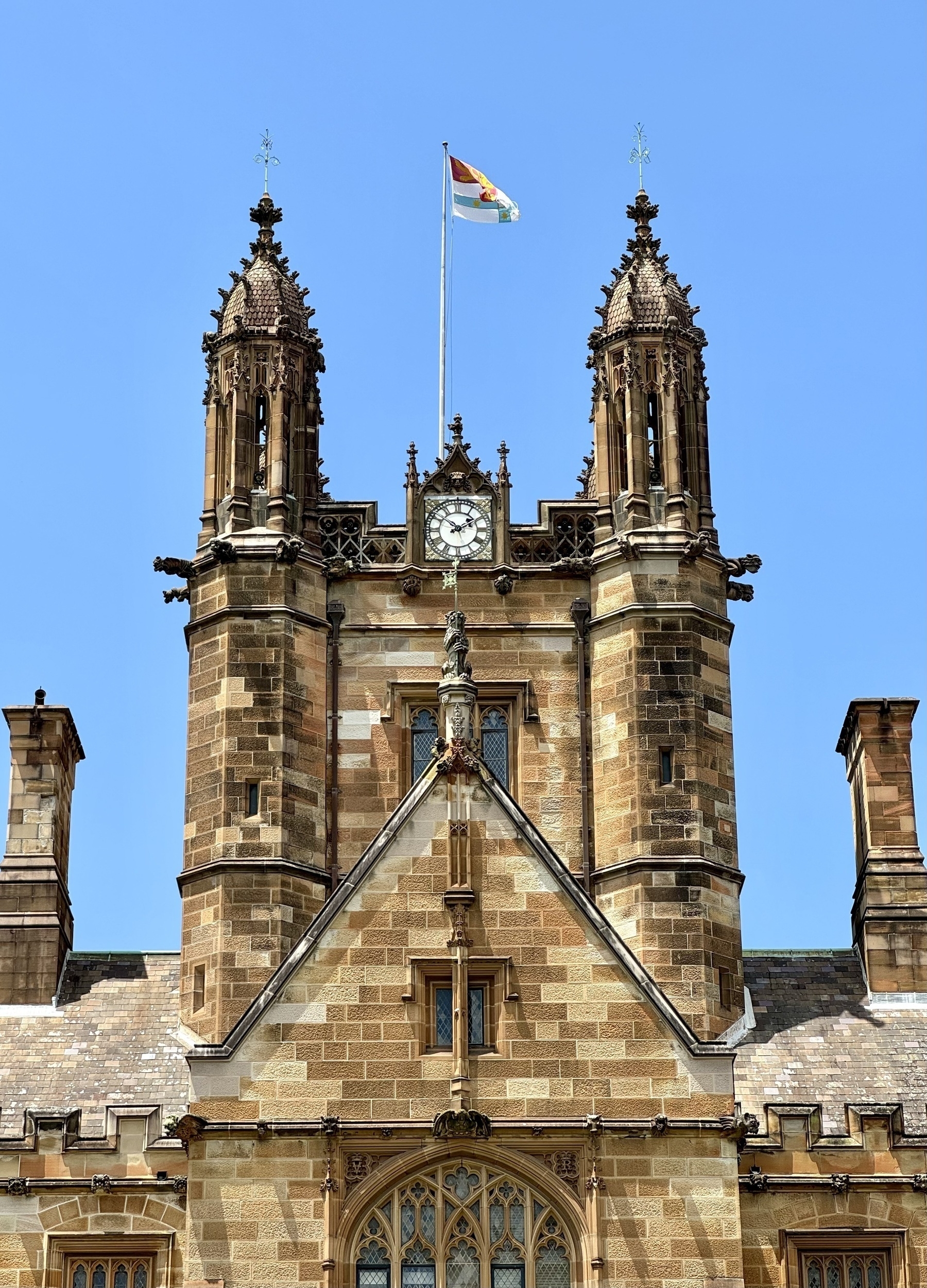 A flag flying from the top of an ornate sandstone tower, with a bright blue sky behind.