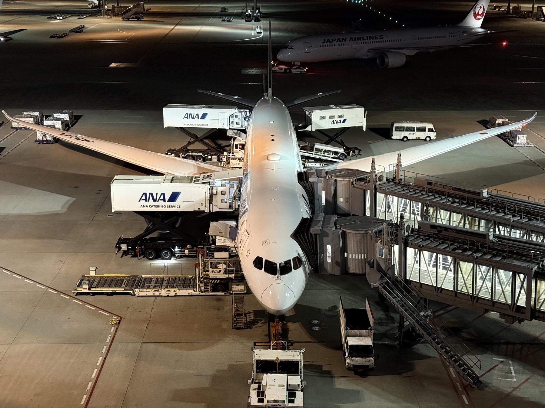 An airplane at a gate at night, with two air bridges attached.