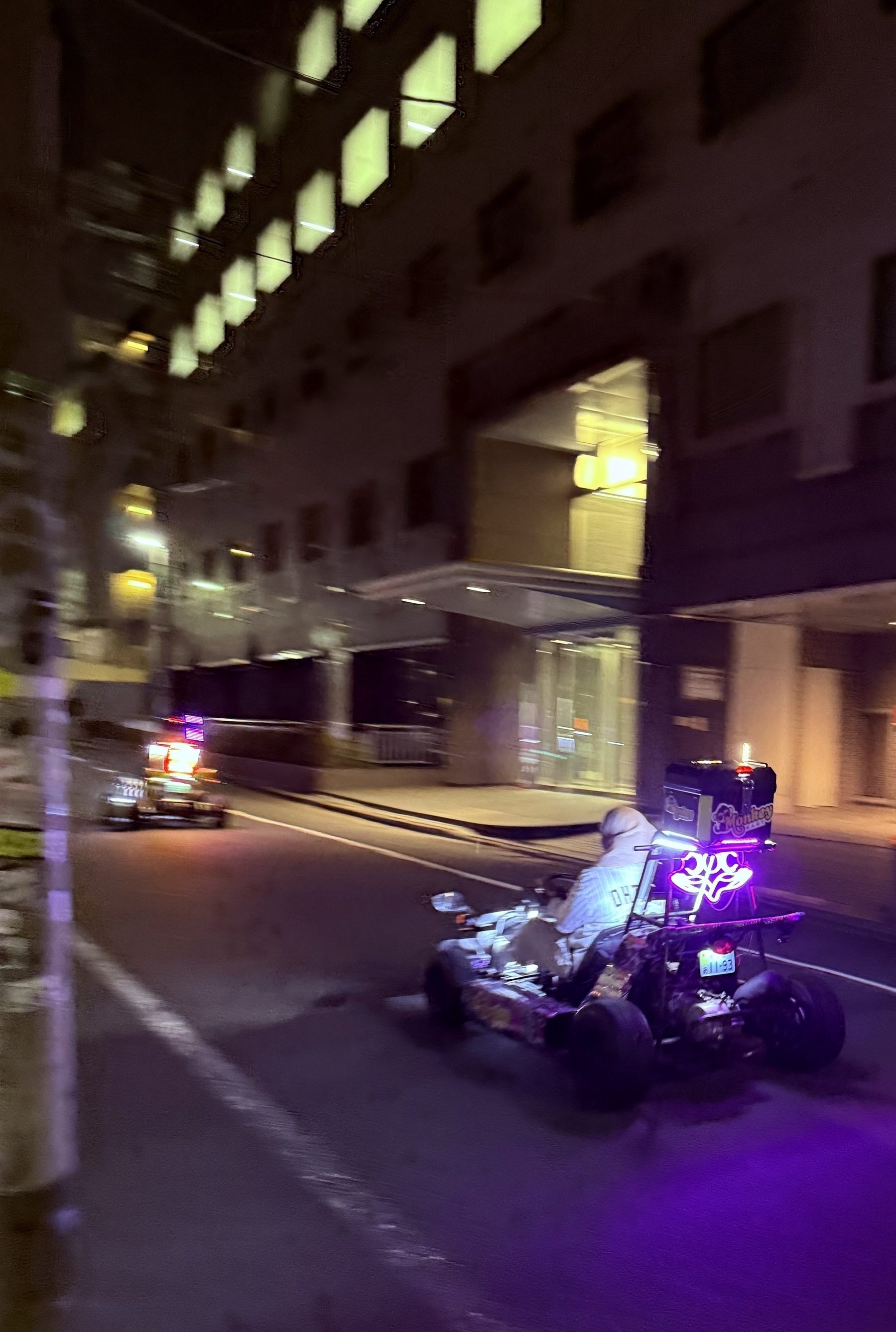 A go kart driving down a street in Shibuya at night.