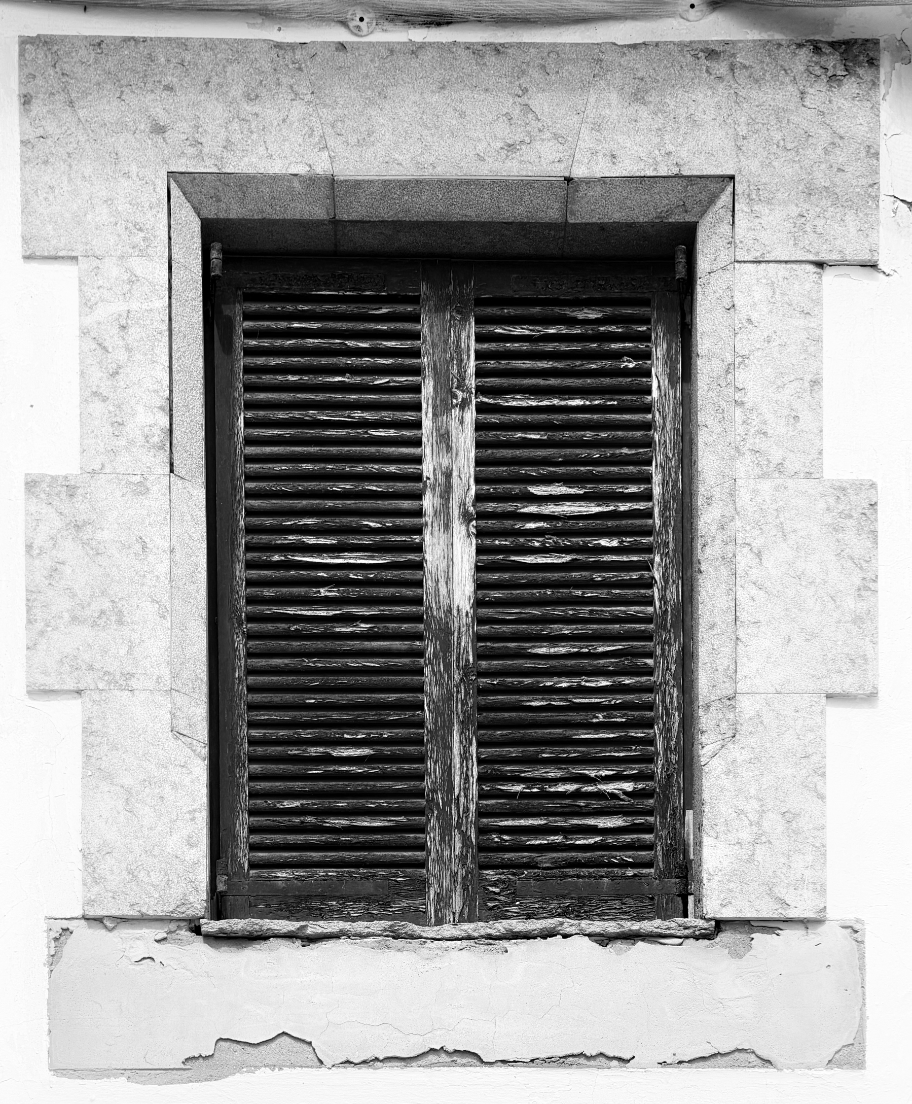 Black and white photo of closed wooden shutters covering a window.