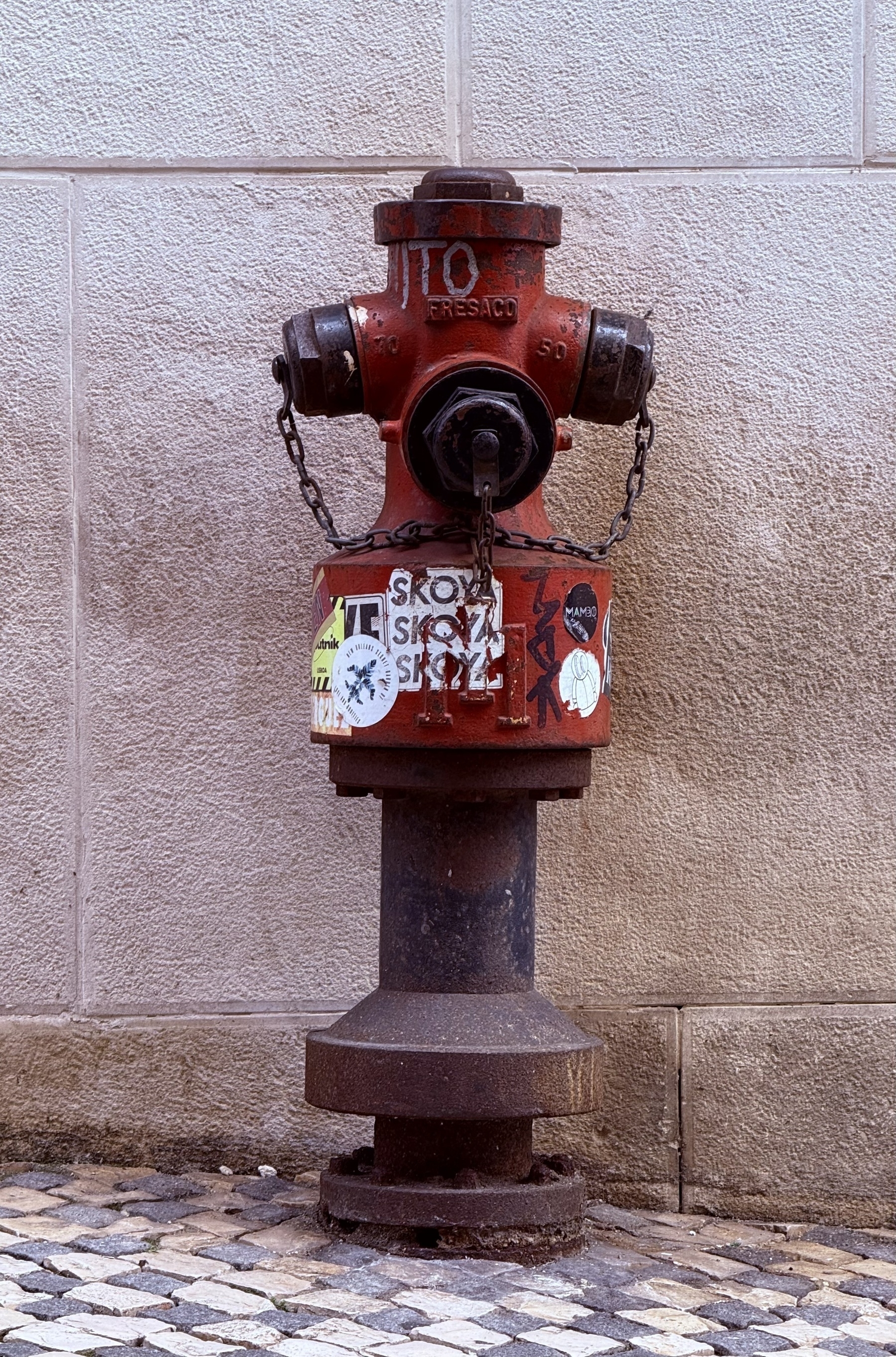 A red fire hydrant against a stone wall, on a cobbled pavement.